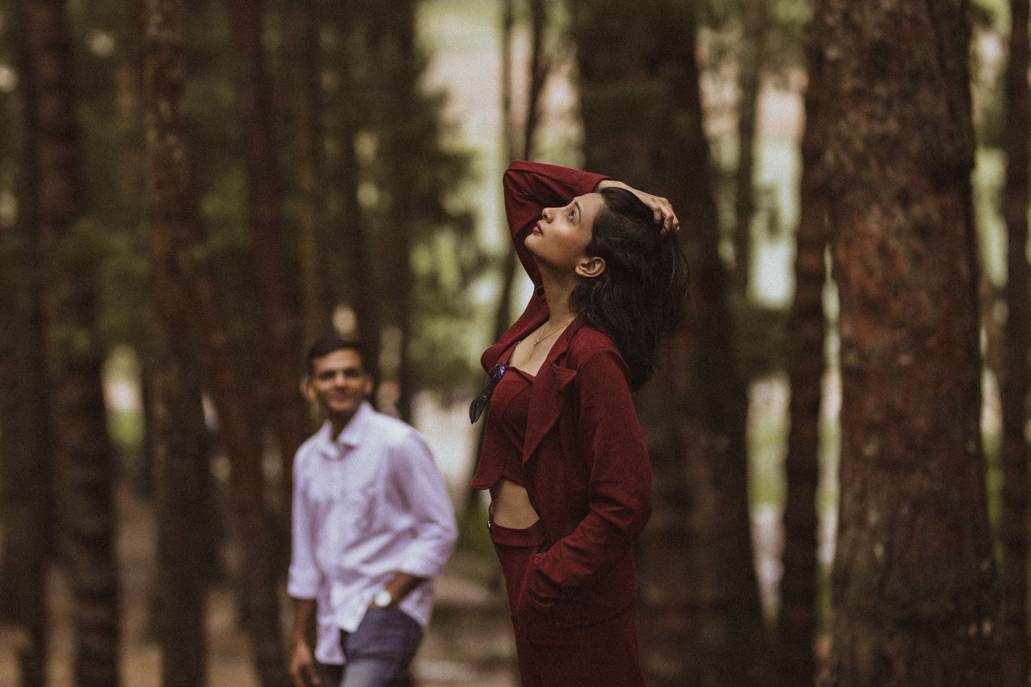 A couple embraces in a romantic moment while standing among tall trees in a forest setting.