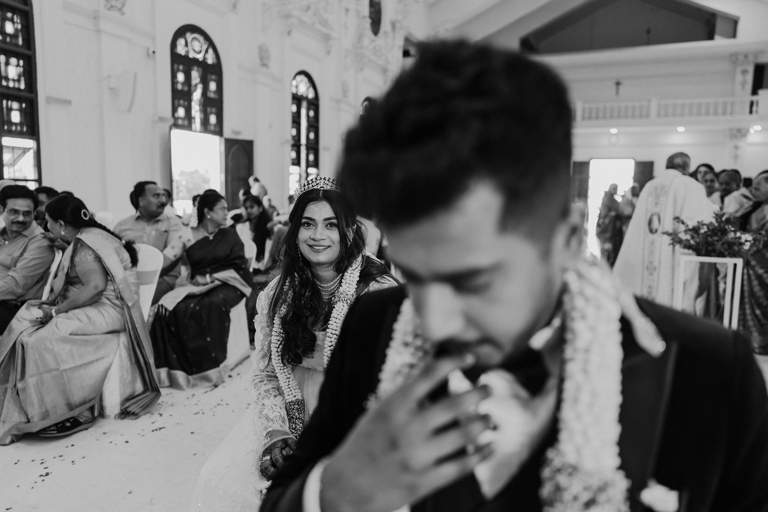 Black and white candid photograph of a wedding ceremony in a church with guests seated in pews in the background.