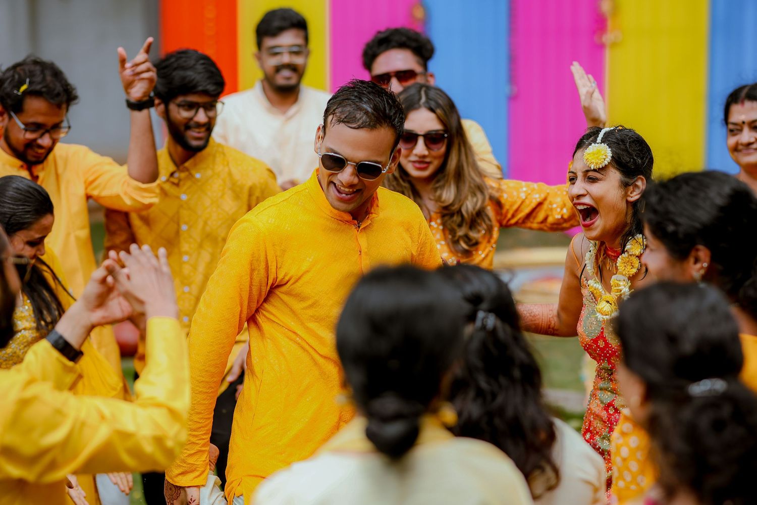 A joyful celebration with people in yellow traditional attire dancing and celebrating during a colorful festival.