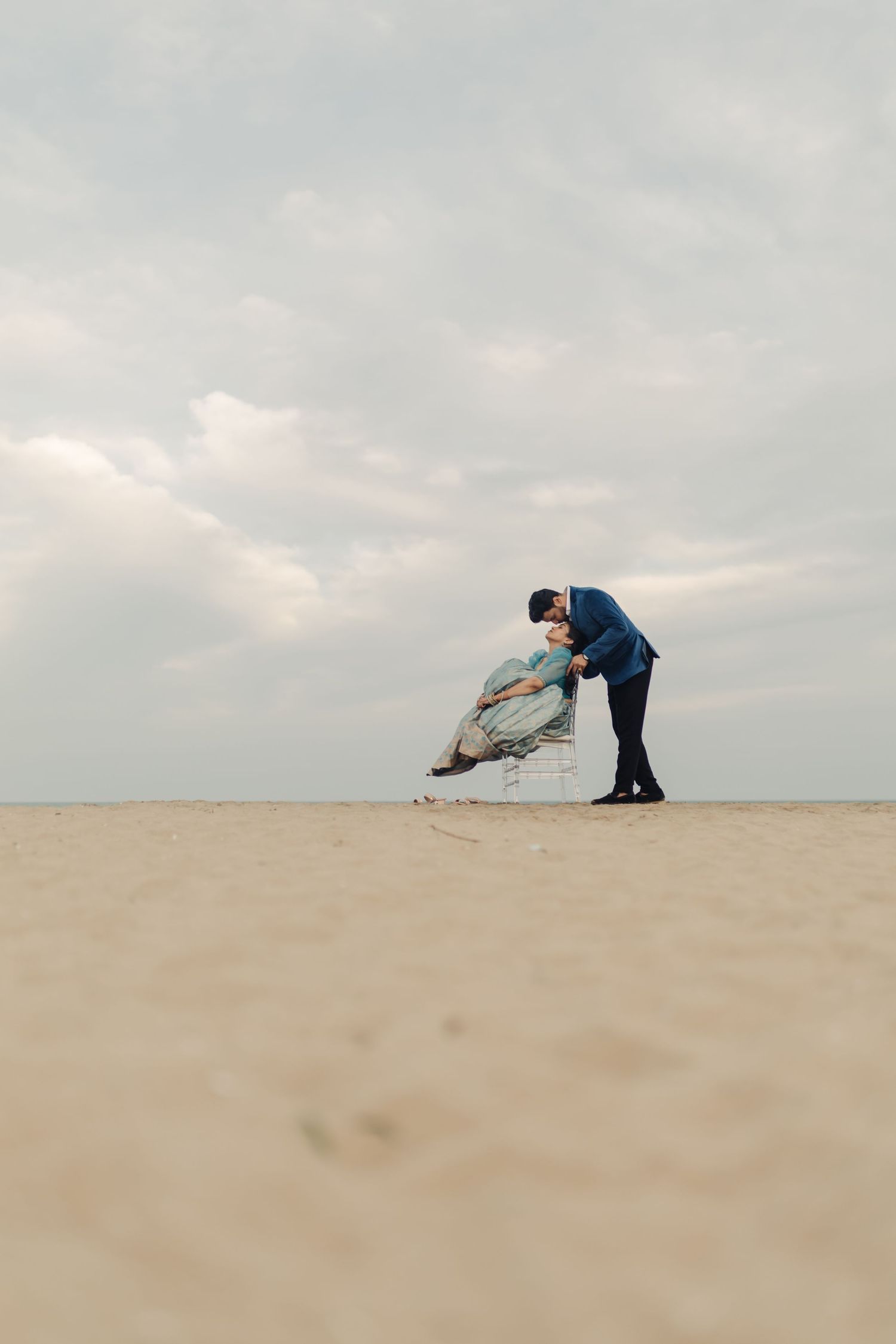 A sequence of images shows two people performing a dynamic dance move on a sandy dune against a cloudy sky.