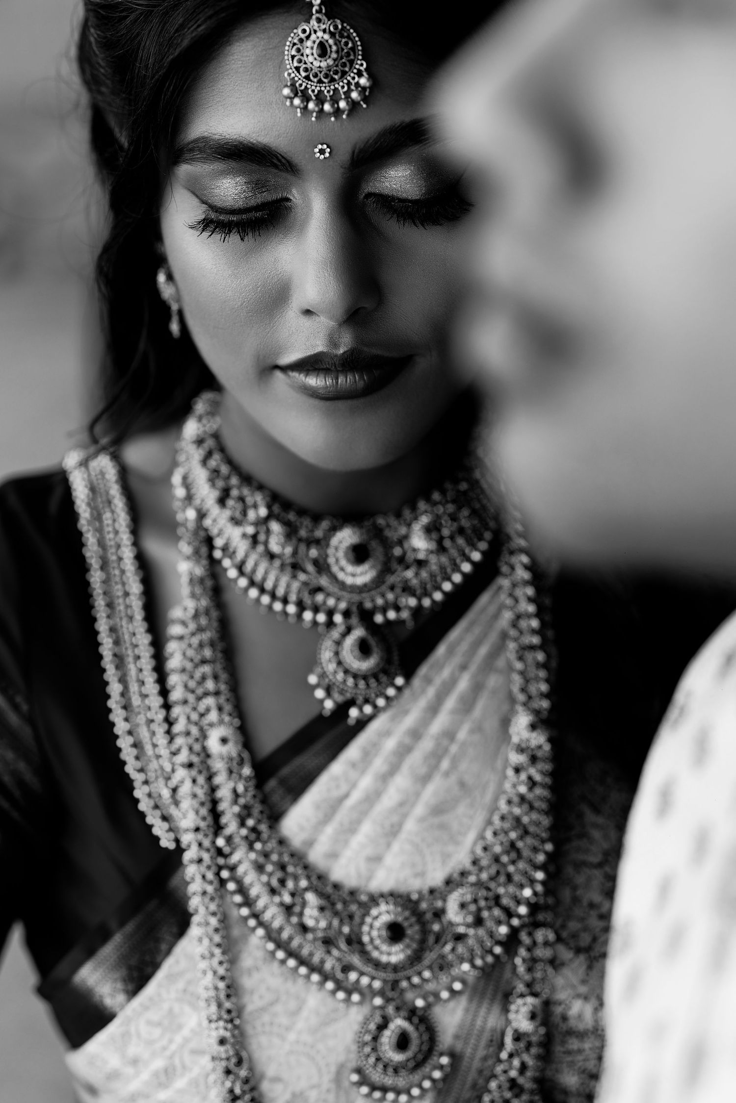 Black and white portrait of an Indian bride in traditional jewelry, saree, and maang tikka with elegant makeup.