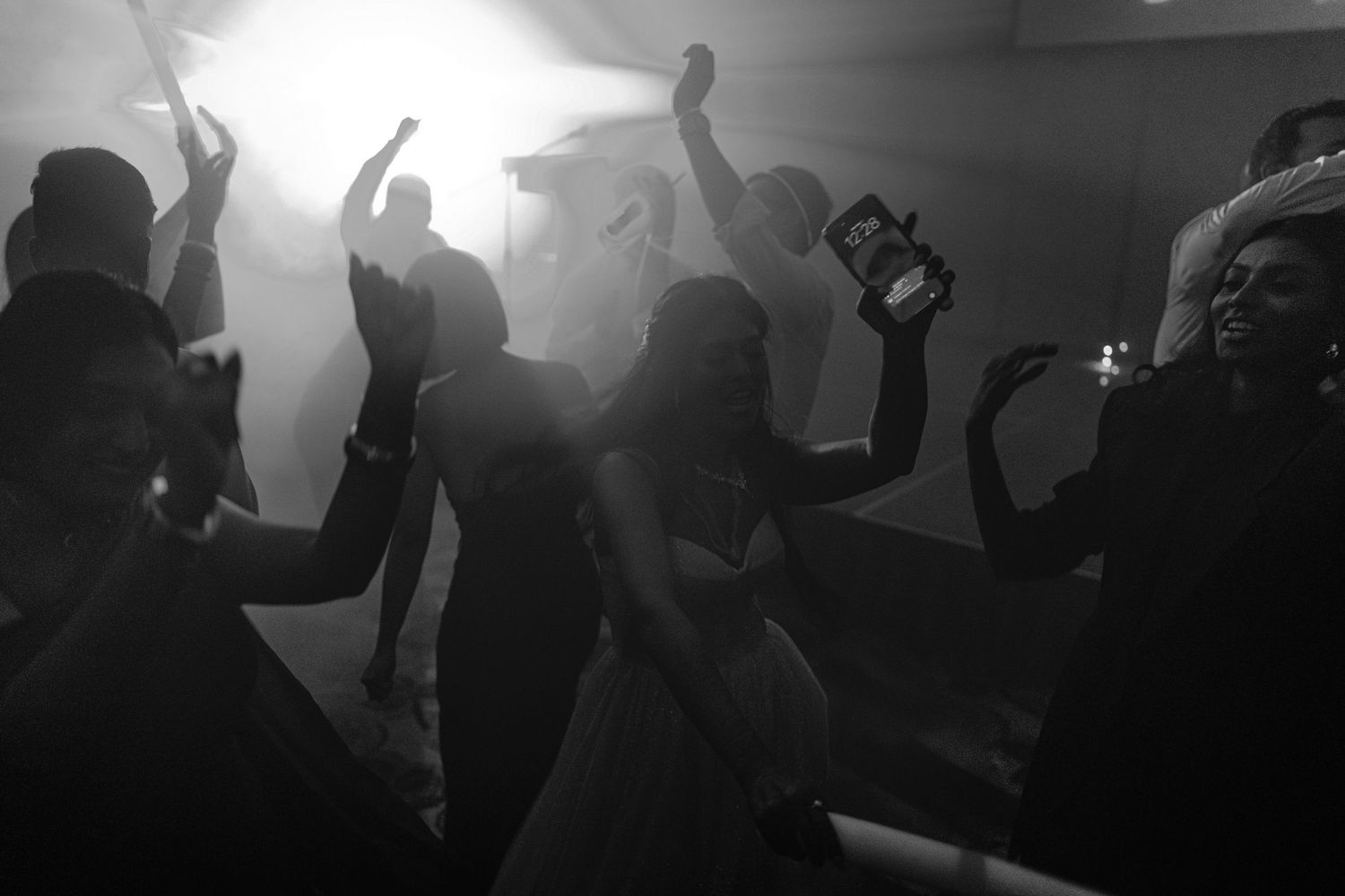 Black and white photo of wedding guests dancing energetically on a dimly lit dance floor.
