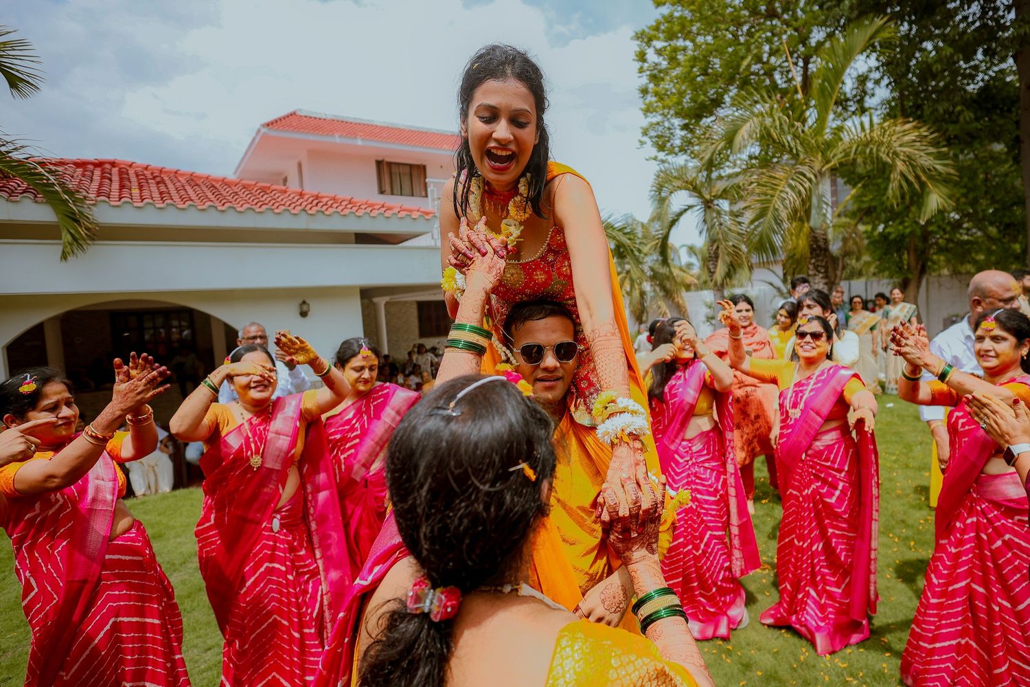 A group of dancers in vibrant pink and red traditional outfits perform a synchronized dance routine outdoors.