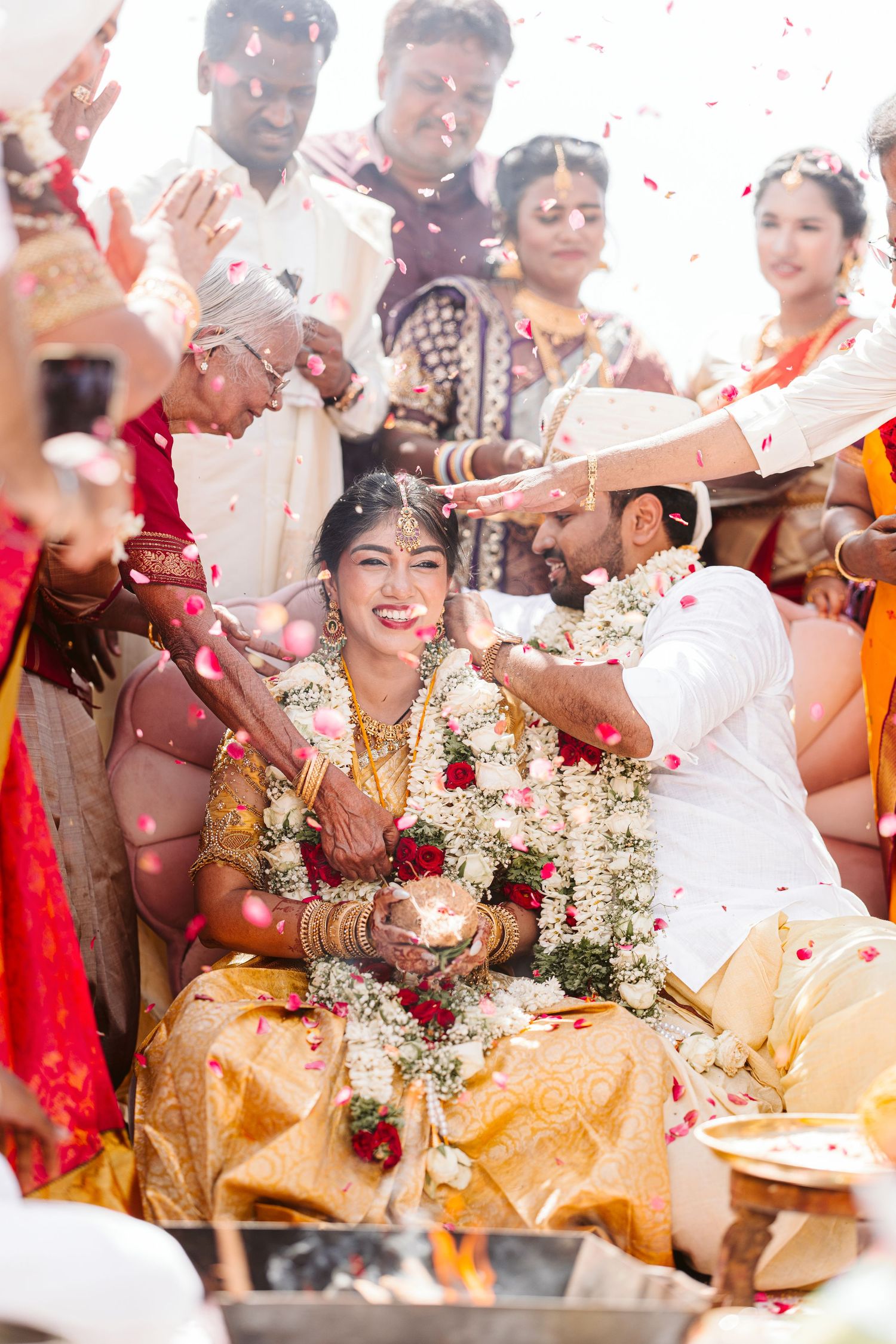 Wedding guests shower flower petals during a traditional Indian ceremony celebration with bright colors and decorations.