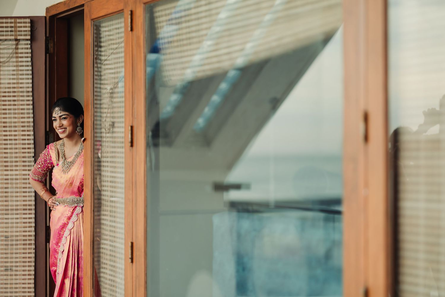 Couple in traditional Indian attire poses together in a modern building interior with glass windows.