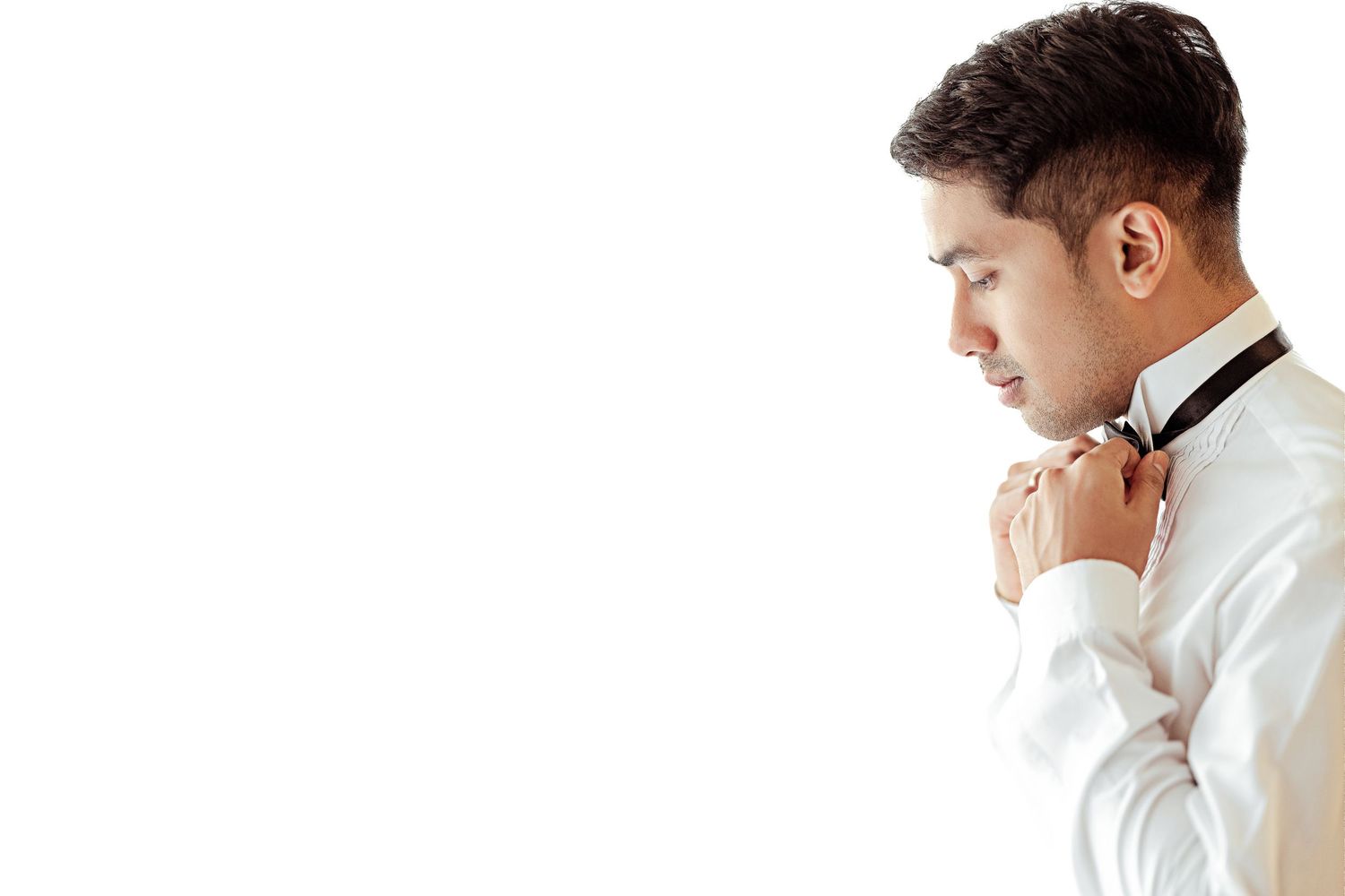 Young man in white dress shirt adjusting black bow tie, side profile view on white background.