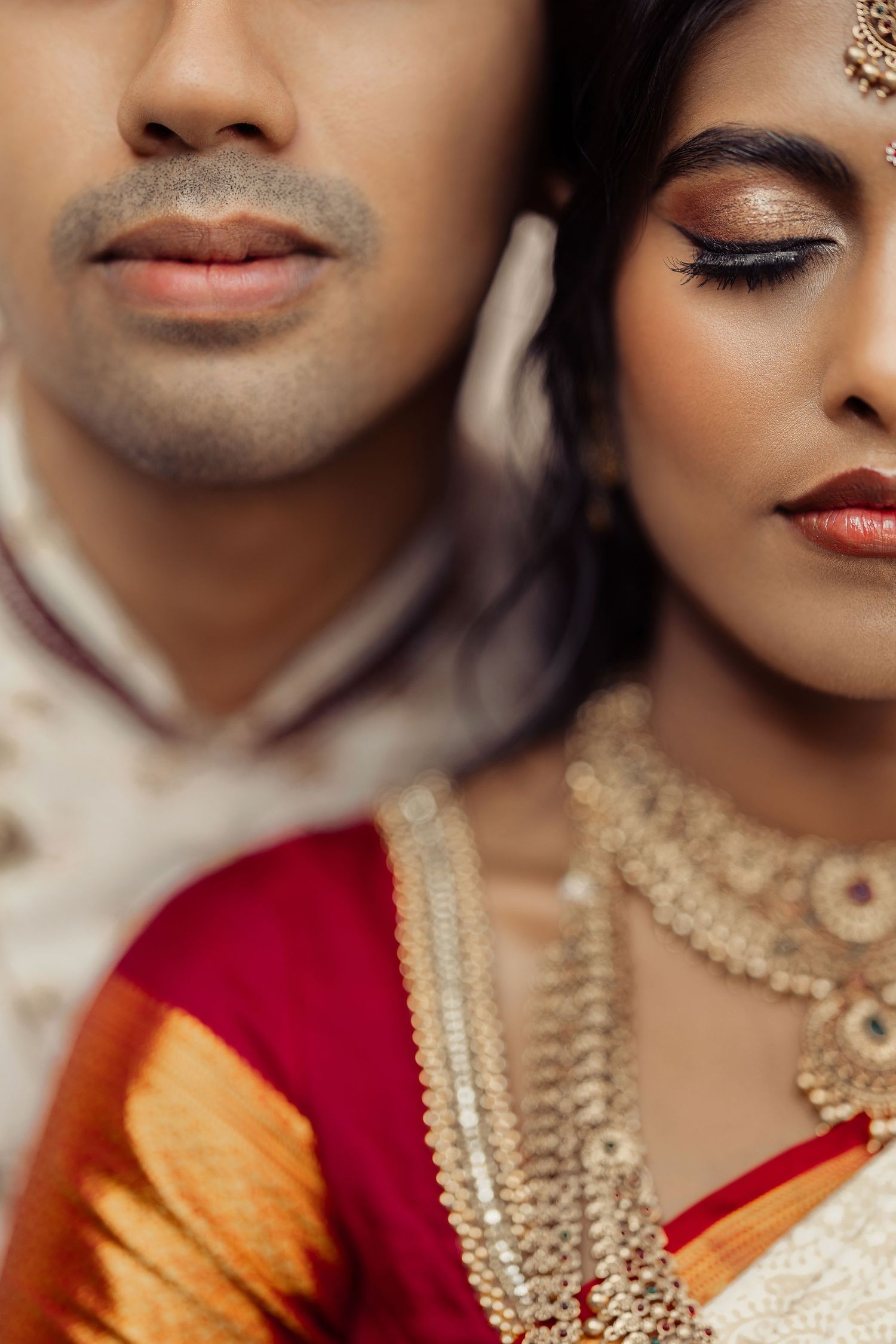 Close-up of Indian bride and groom in traditional wedding attire, bride wearing gold jewelry and red saree.