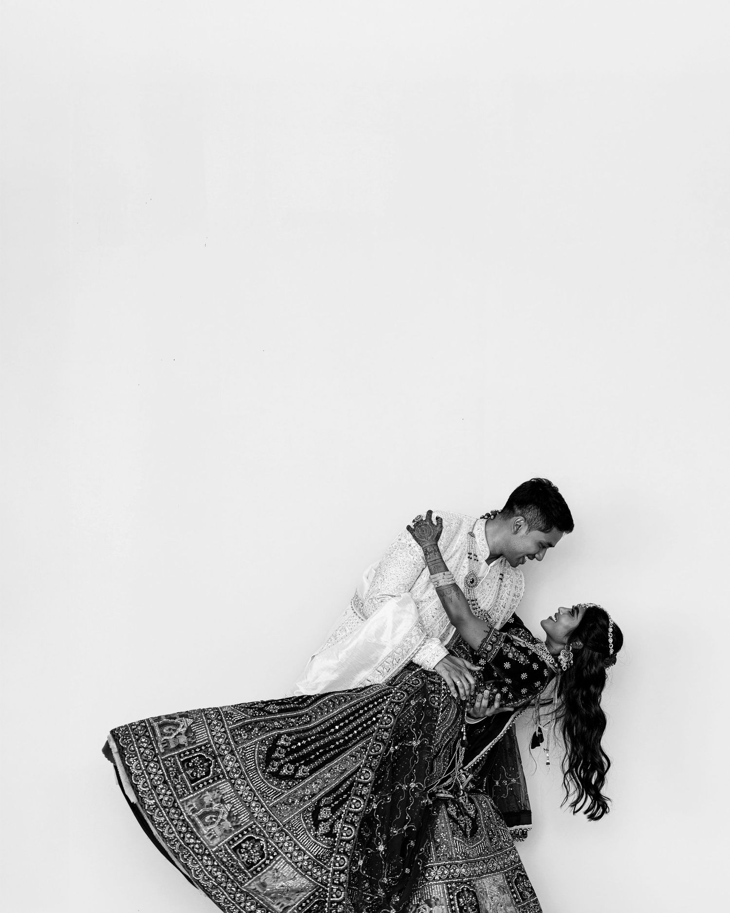 Black and white photo of a couple dancing romantically, woman in ornate flowing skirt, man in white shirt, studio setting.