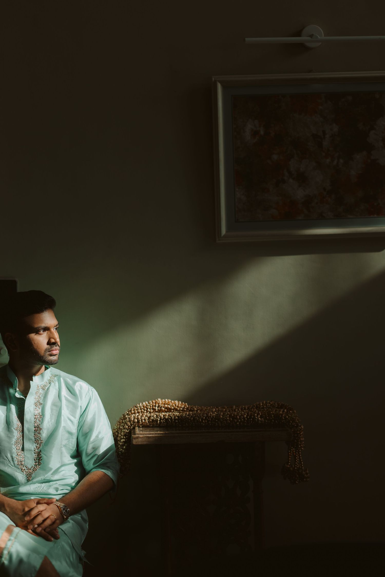 Dramatic moody portrait of person in mint green shirt sitting against dark wall with directional lighting.