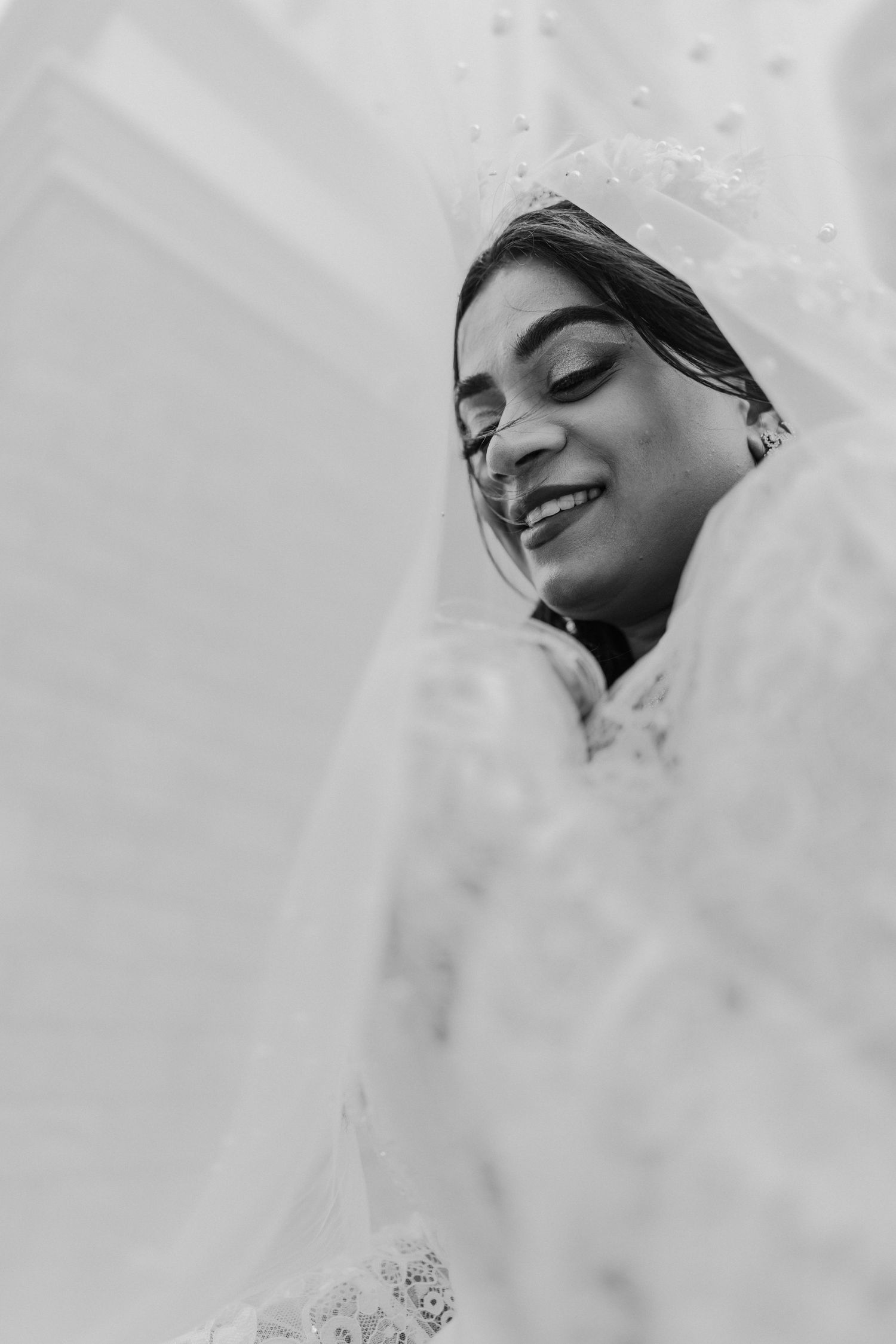 Ethereal bridal portrait through delicate white veil in soft light.