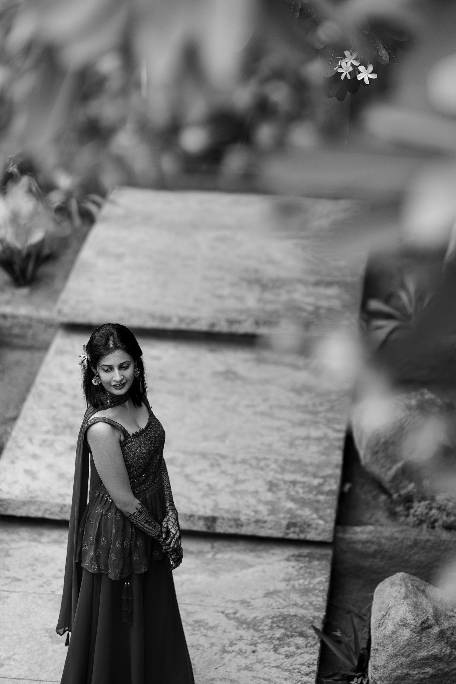 A figure in a flowing black dress stands outdoors in a moody black and white artistic portrait series.