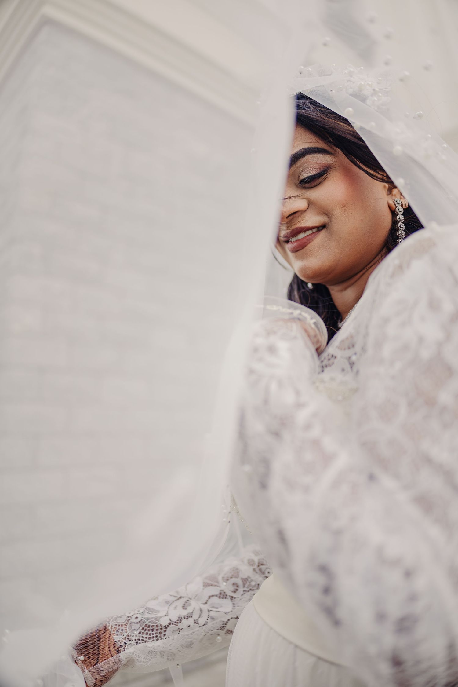 Close-up artistic bridal portrait showing delicate white lace veil details in soft lighting.