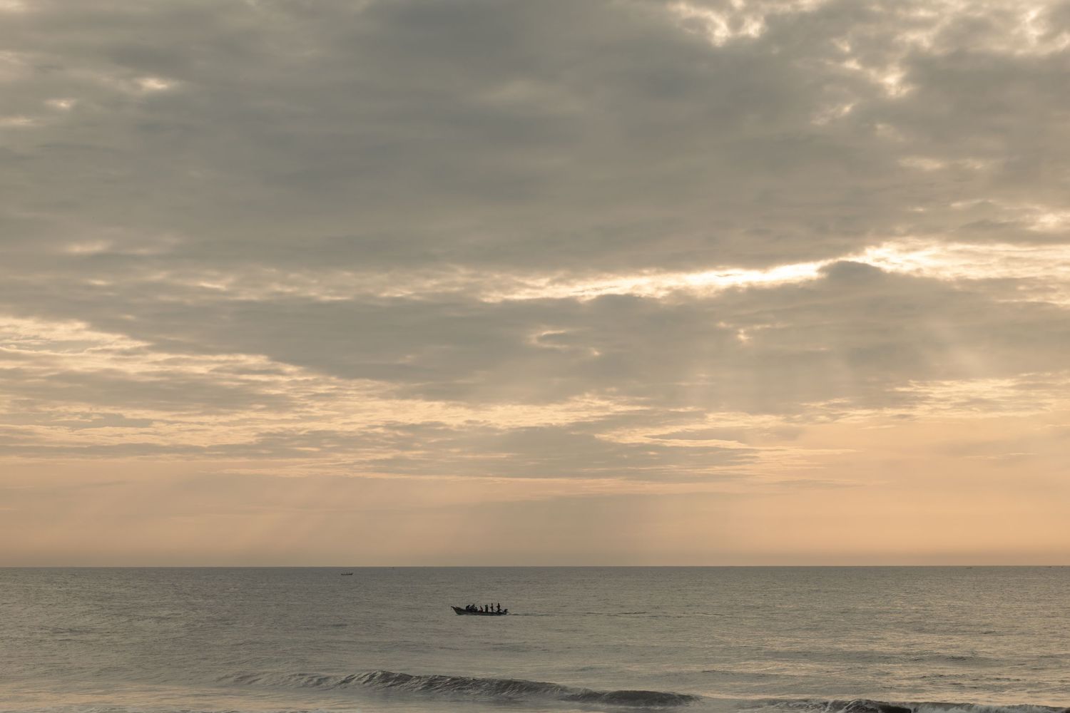 Dramatic cloudy sunset over ocean horizon with silhouetted fishing boat in distance.
