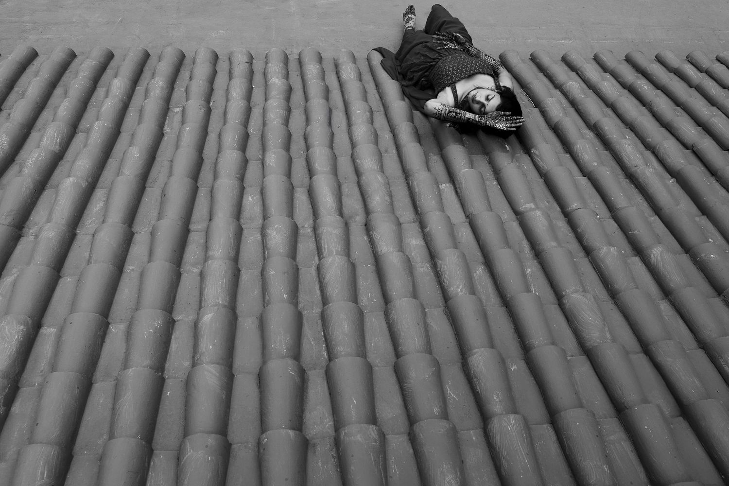 A person lies on their back atop gray corrugated metal roofing, creating a striking geometric pattern.