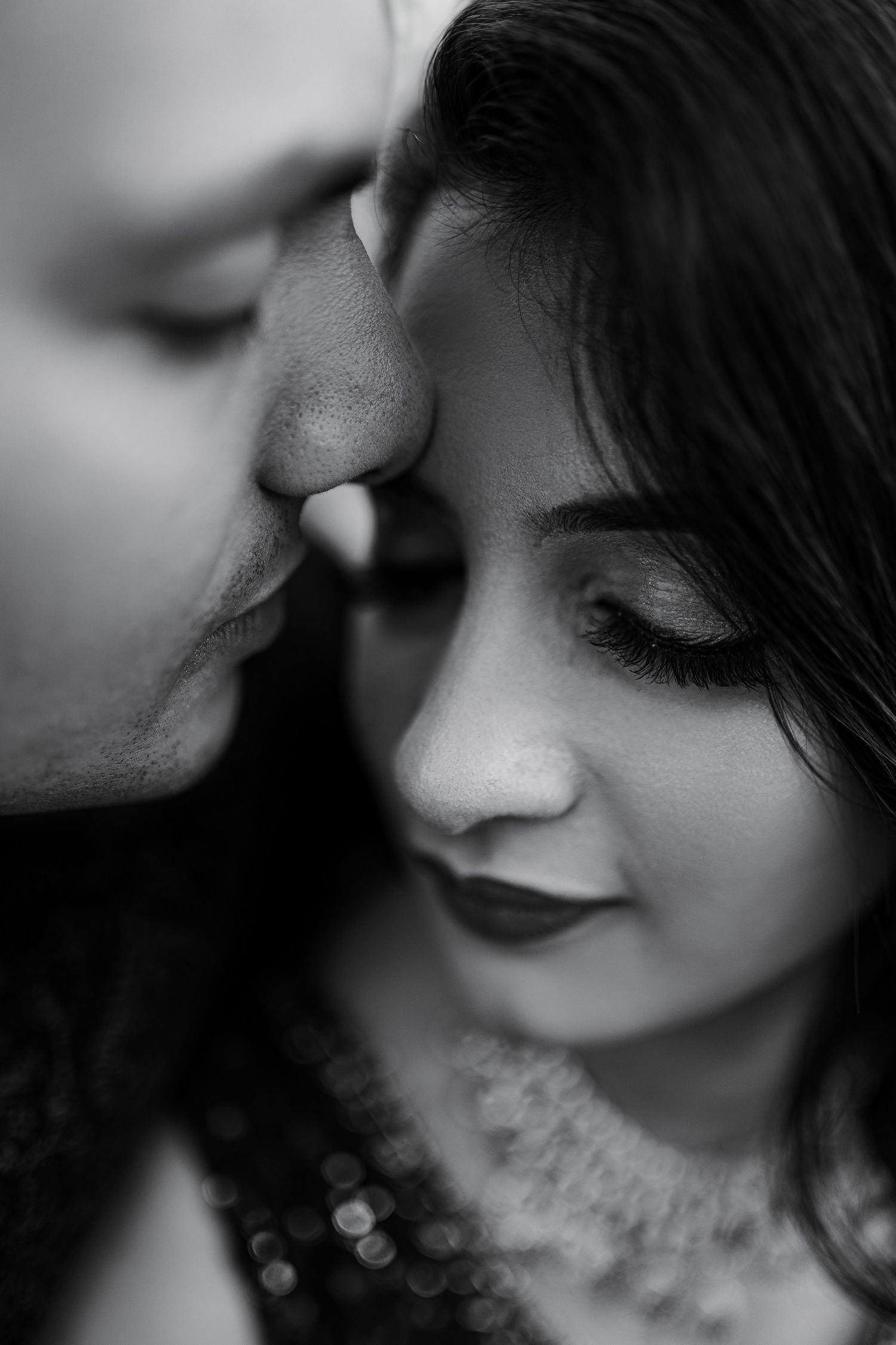A romantic black and white close-up photo showing tender intimacy between two people with soft lighting and shallow depth of field.