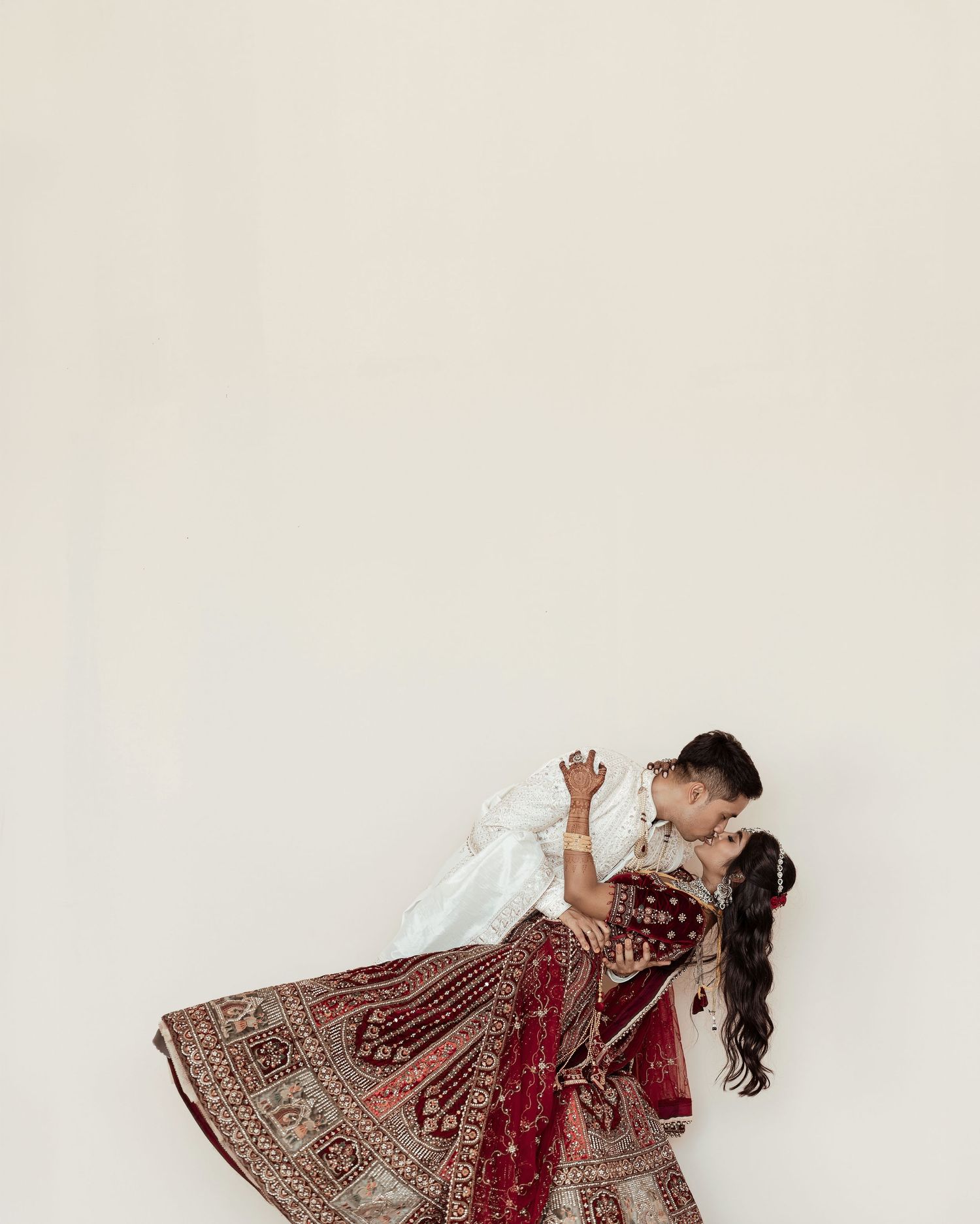 Couple sharing a romantic dip kiss in traditional Indian wedding attire, bride in red lehenga.