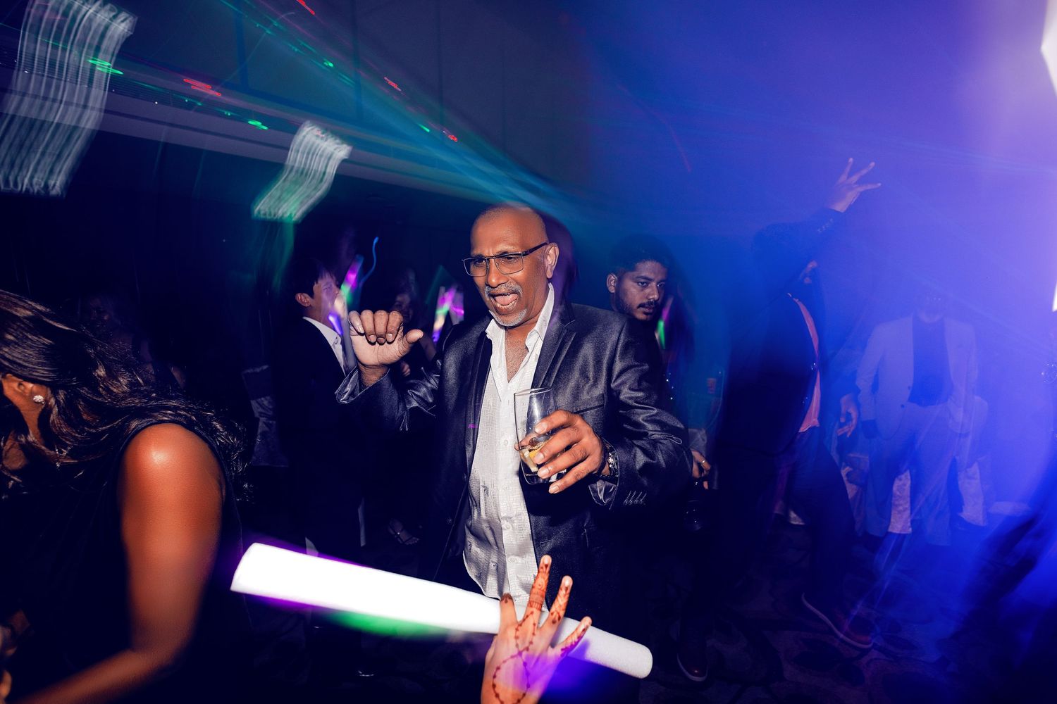 Man dancing at a vibrant nightclub party with colorful laser lights and crowd in the background.