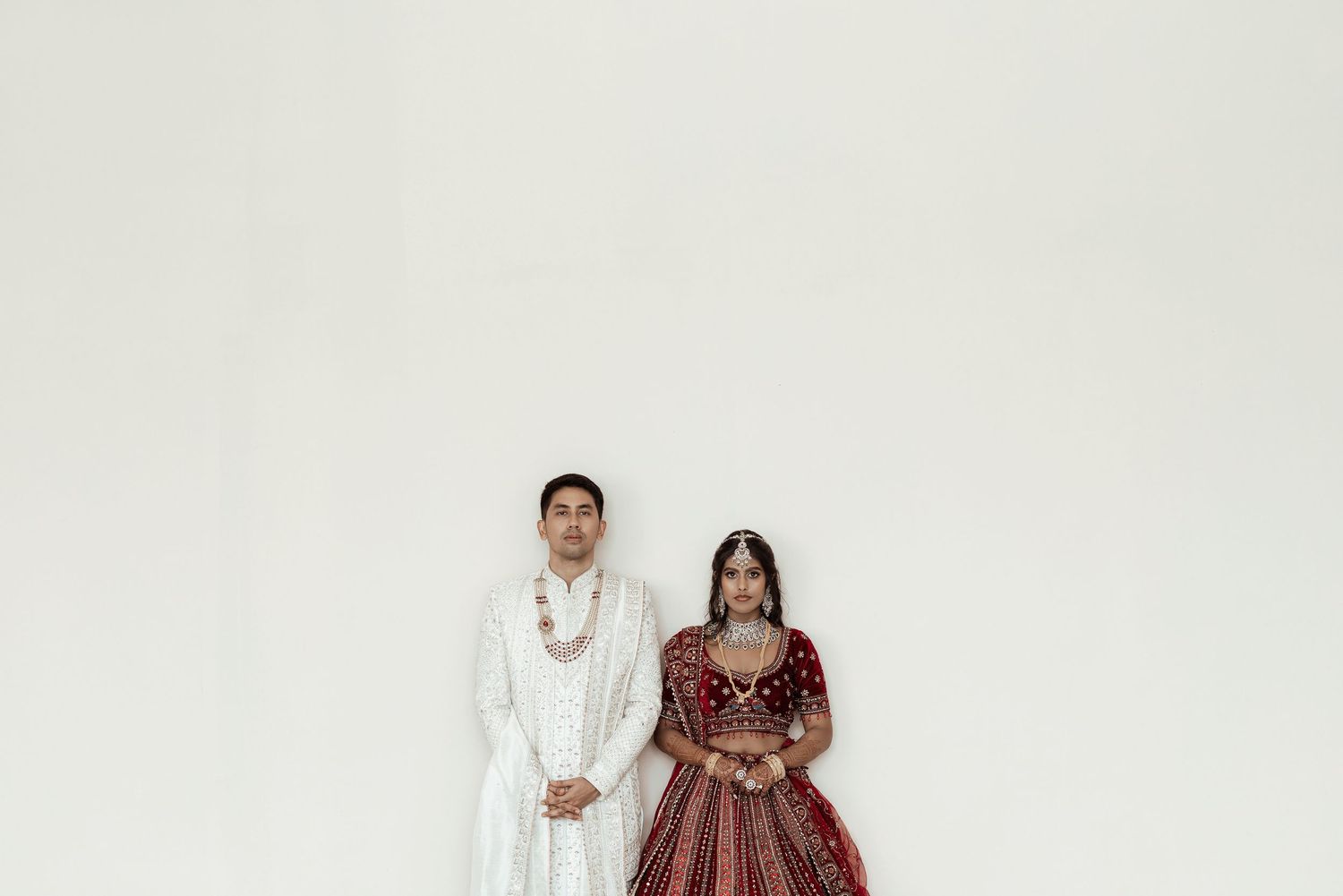 Indian couple in traditional wedding attire, groom in white sherwani and bride in red lehenga.