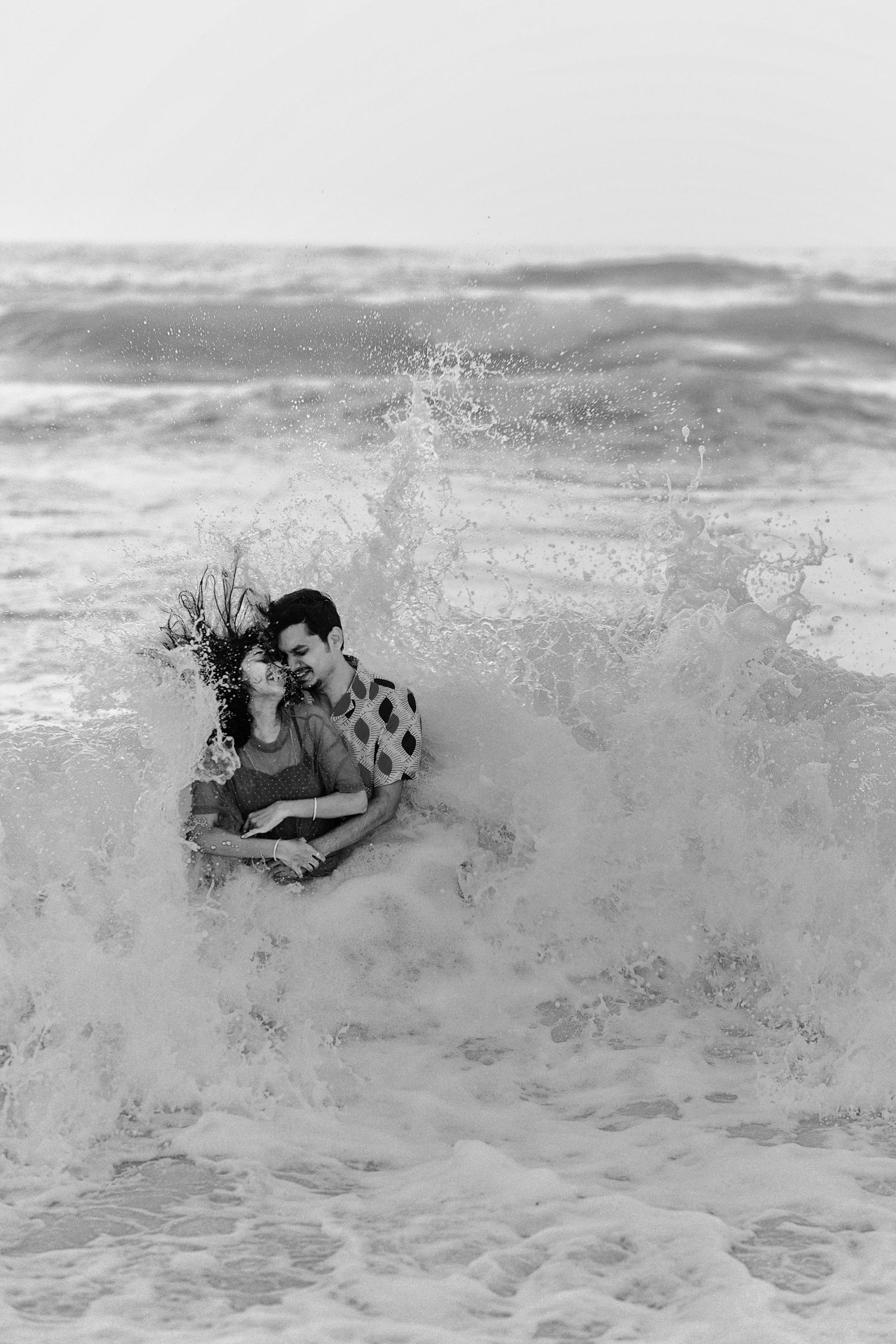 Black and white photo of waves crashing over swimmers at the beach.