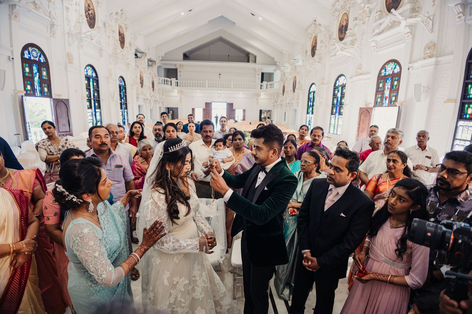 Wedding ceremony in a bright church with stained glass windows and gathered guests.