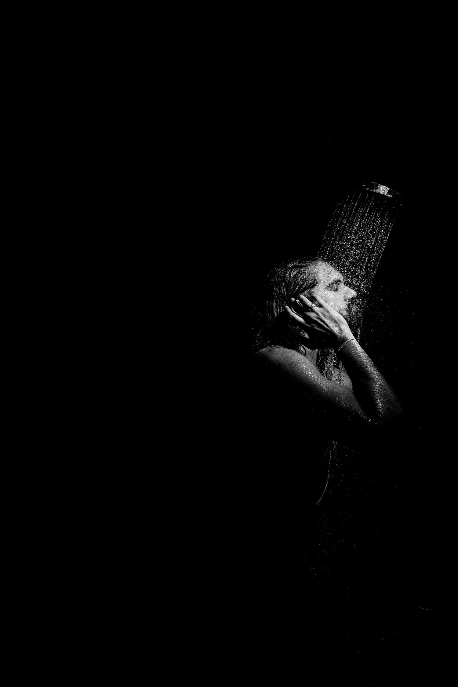 Black and white artistic portrait showing dramatic lighting and shadows in a dark studio setting.