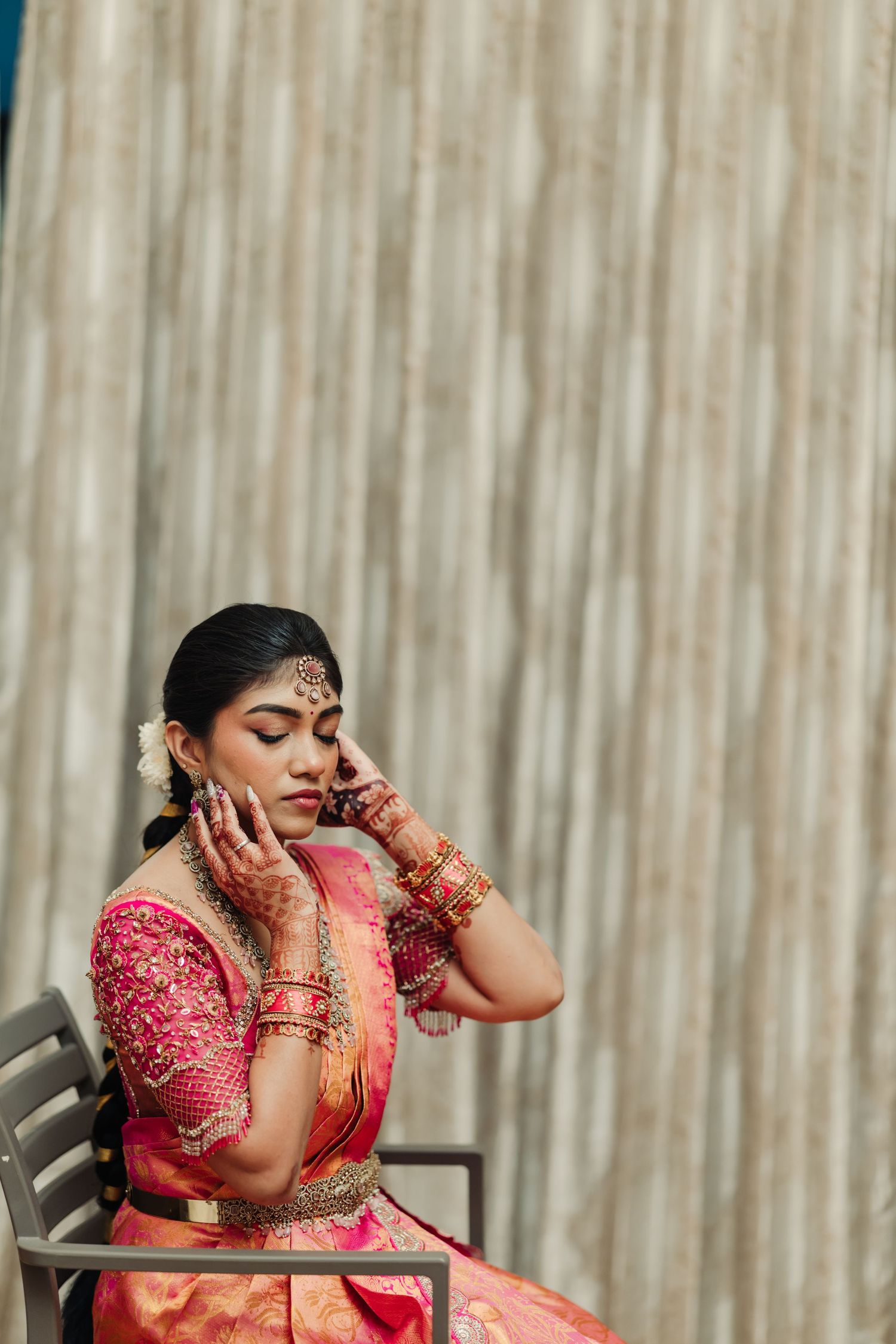 Woman in red traditional Indian attire with henna decorated hands poses emotionally in a chair.