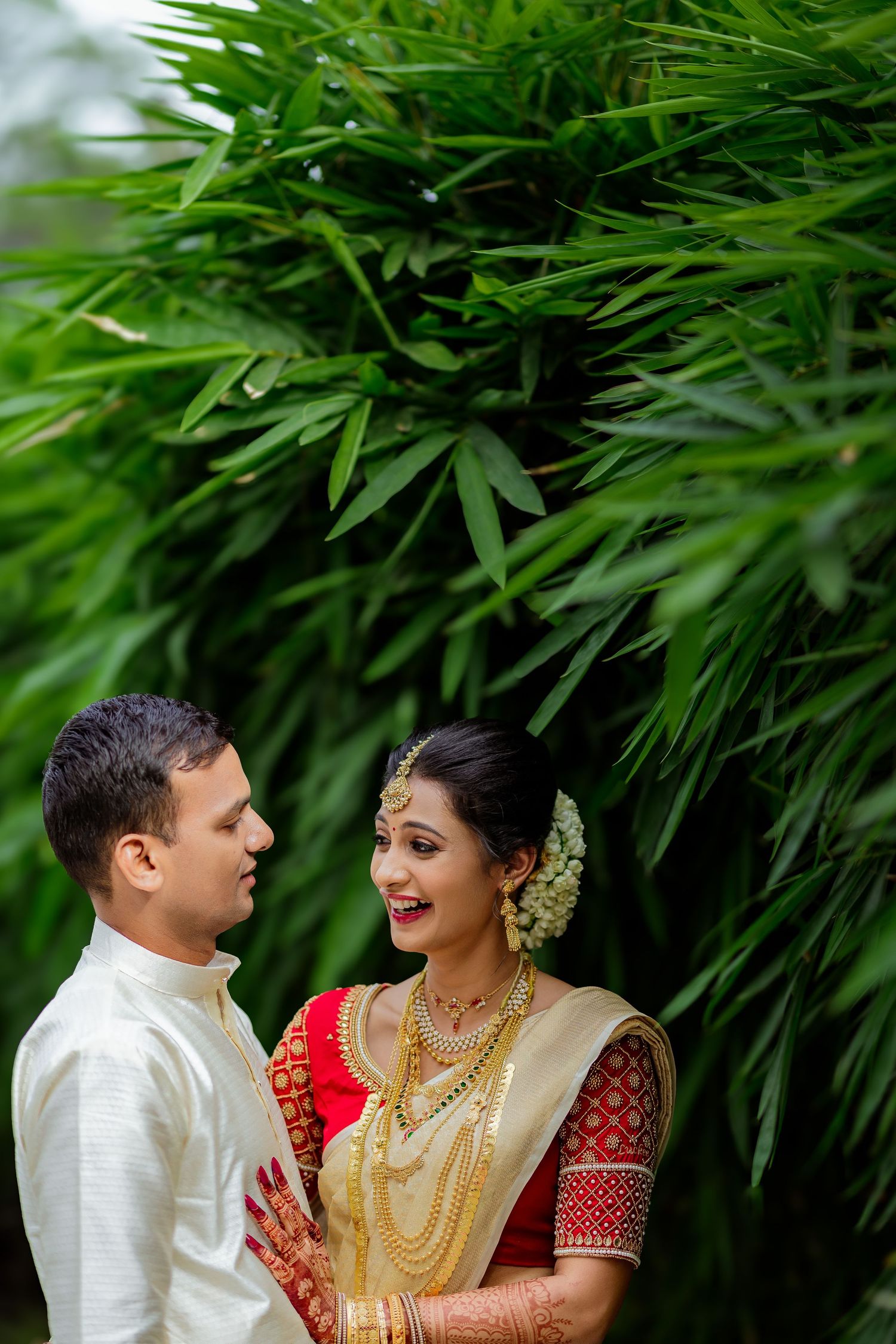 Wedding couple in traditional South Asian attire share intimate moment against lush bamboo garden backdrop.