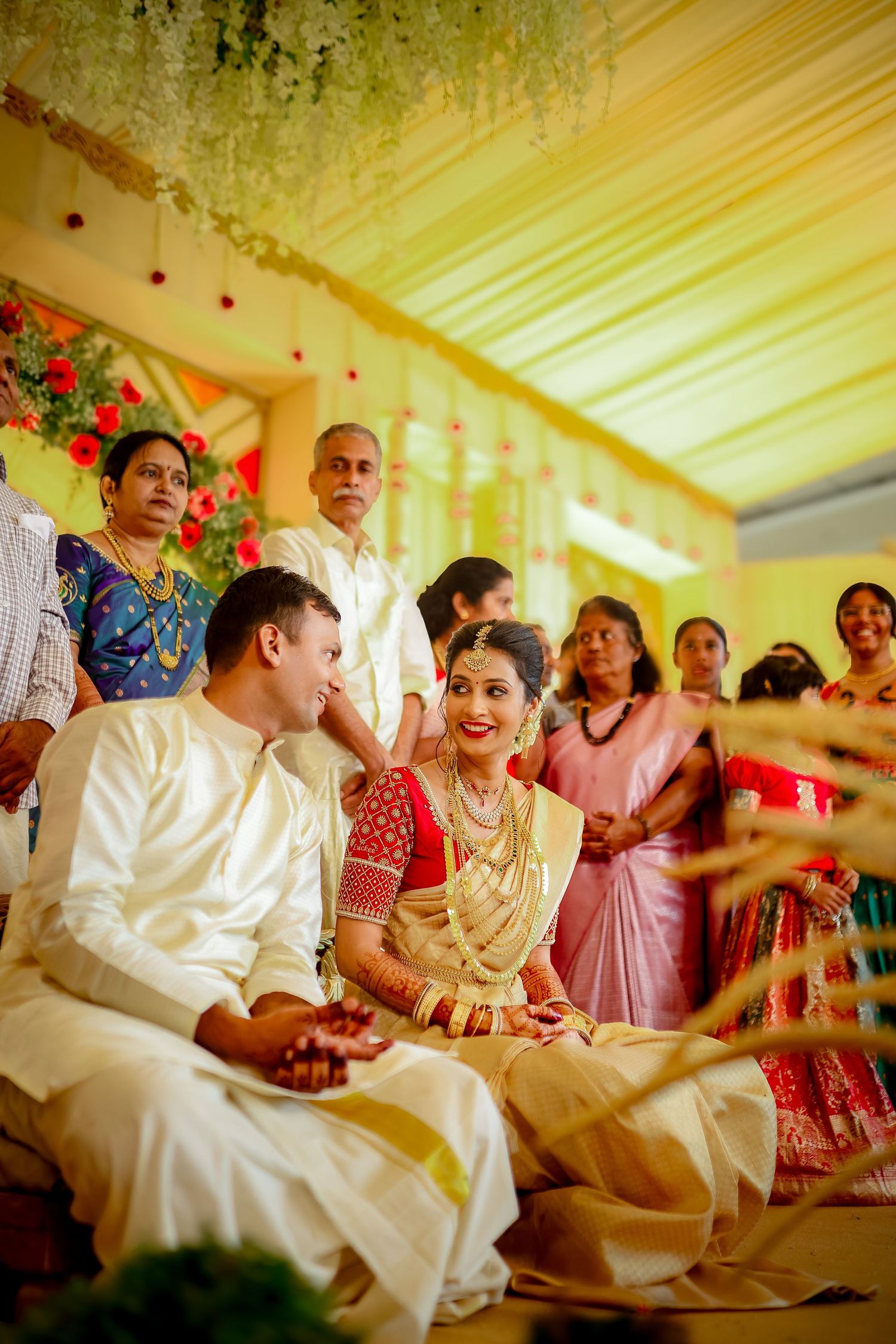 A traditional Indian wedding ceremony shows guests and couple sitting under a decorated tent with yellow draping.