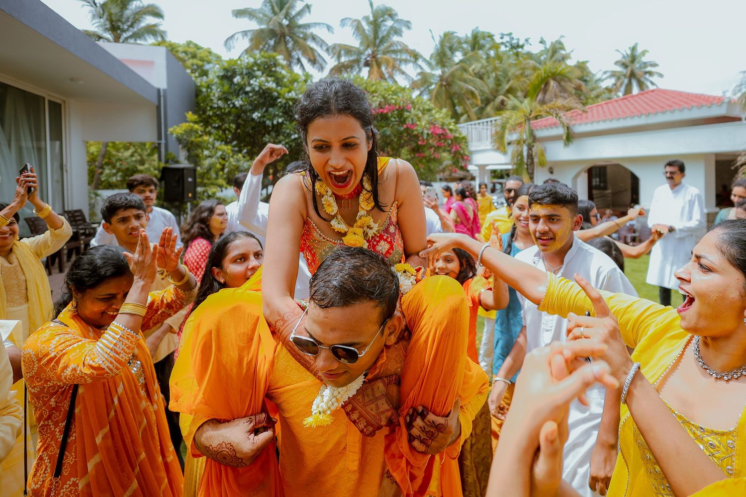 Group of people in bright yellow shirts celebrate during a traditional festival with palm trees in the background.