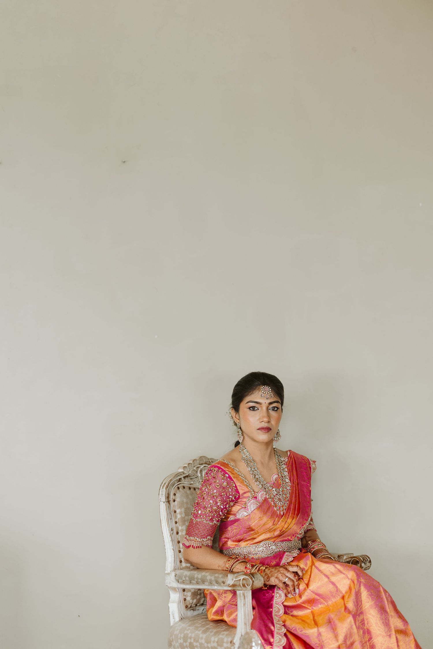 A person in traditional Indian attire sits on a white chair in multiple poses showing different angles of the outfit.
