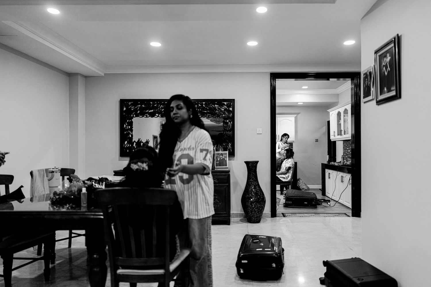 Black and white photo of a woman standing in a modern living room, with another person visible in the background.
