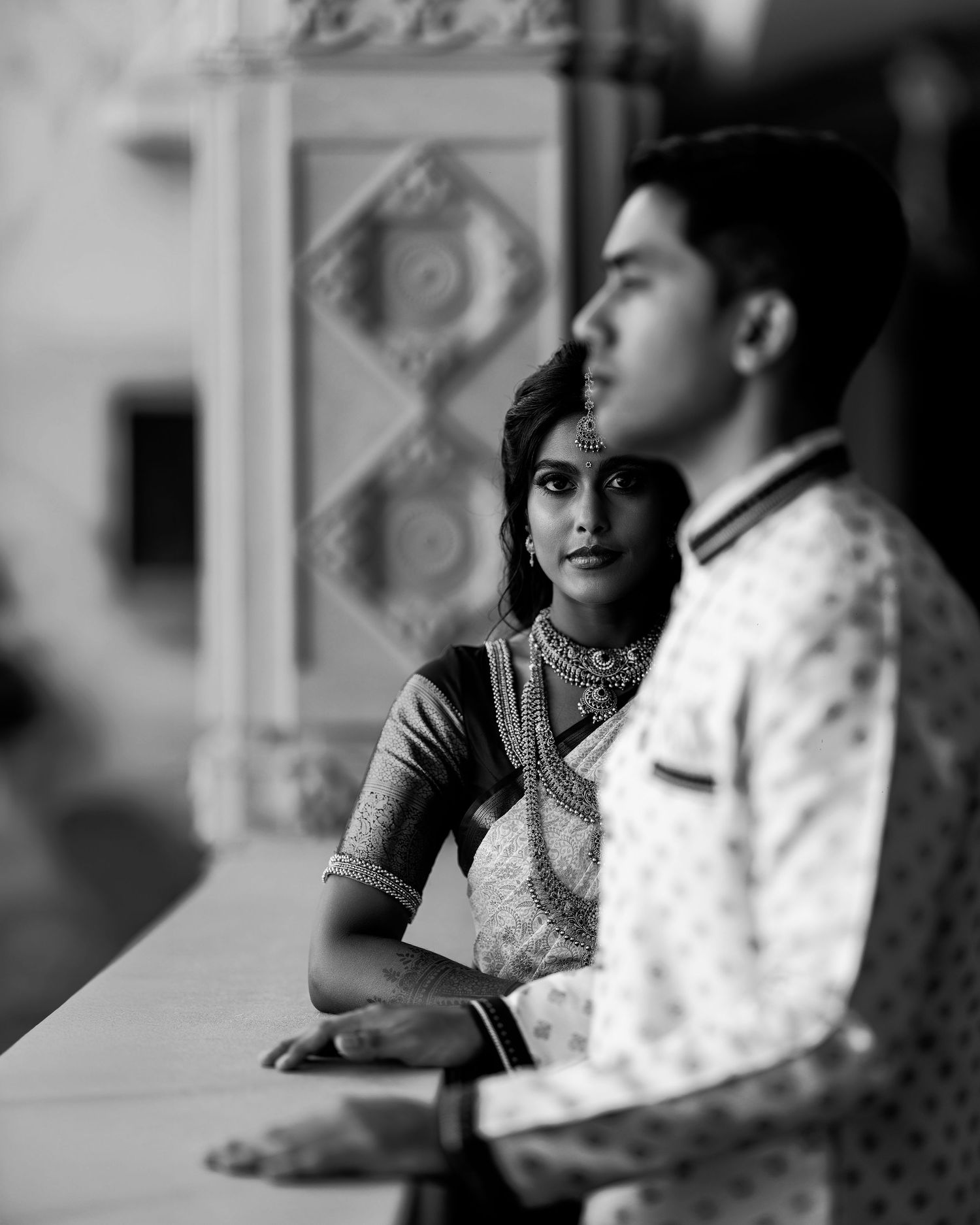 Black and white photo of an Indian couple in traditional attire at an ornate heritage venue during a pre-wedding shoot.