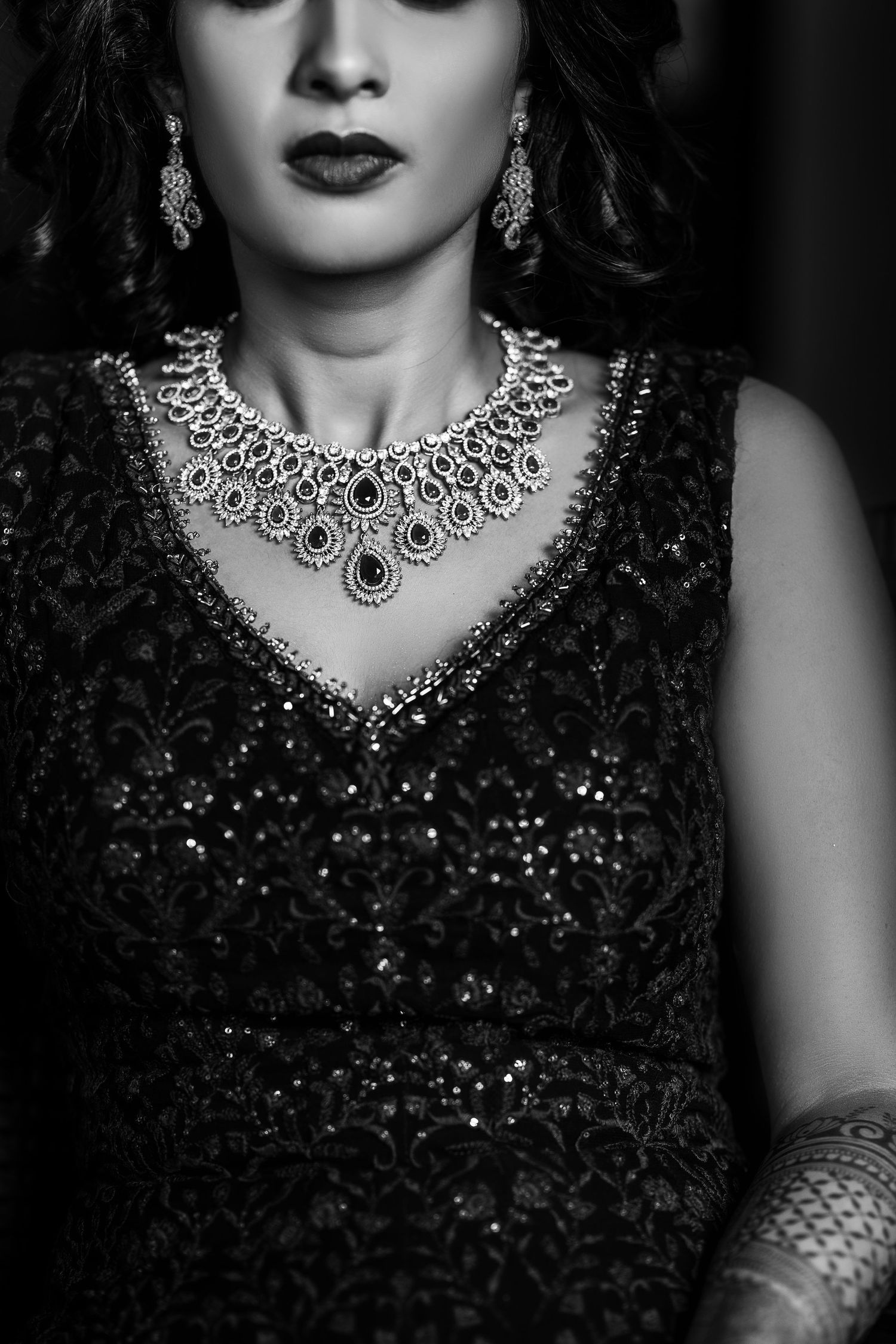 Black and white photo showing an ornate diamond necklace and sparkly dress with dark lipstick and dangling earrings.