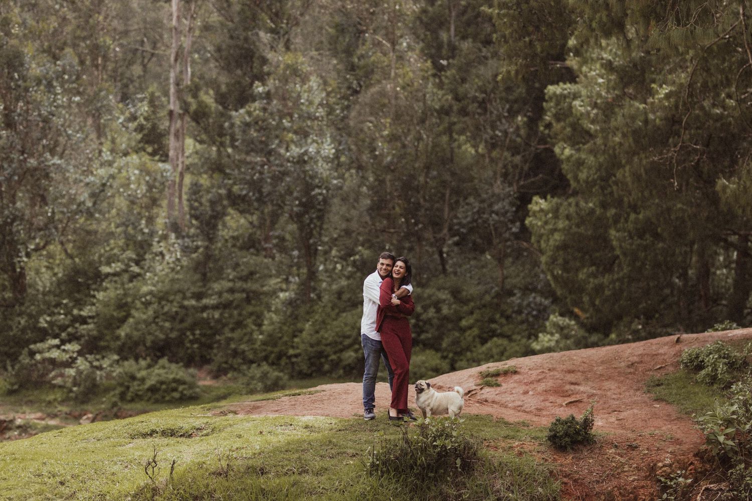 Two people share an intimate moment while sitting on a rustic dirt path with trees in the background.