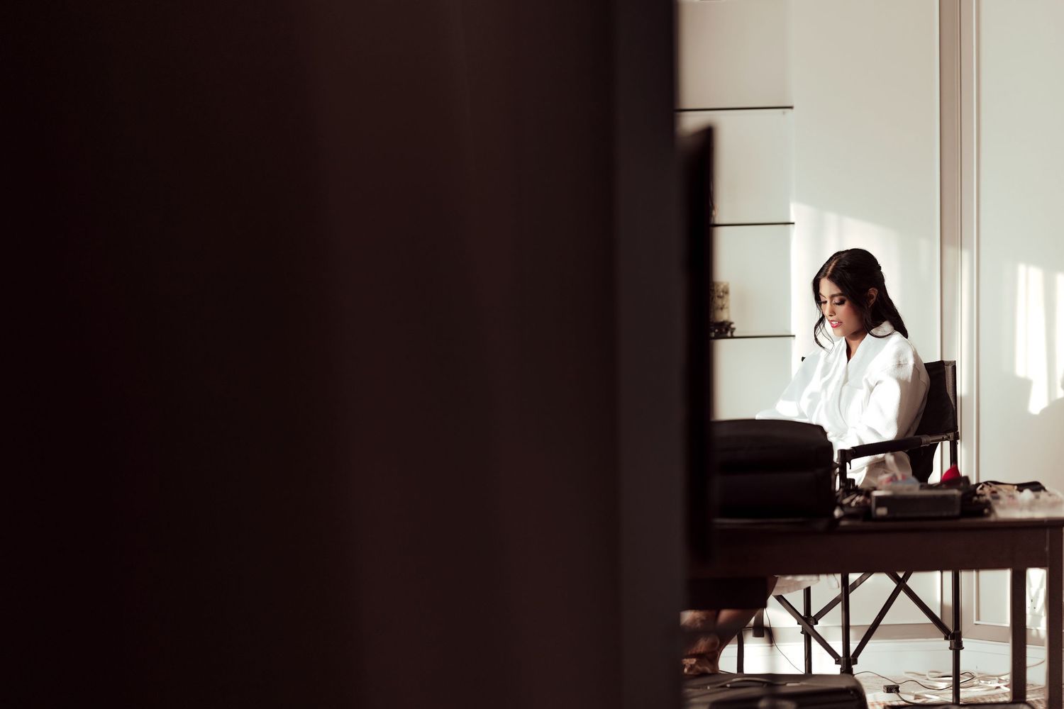 A professional woman in a white shirt sits at a dark wooden desk, focused on work in a bright, elegant office.