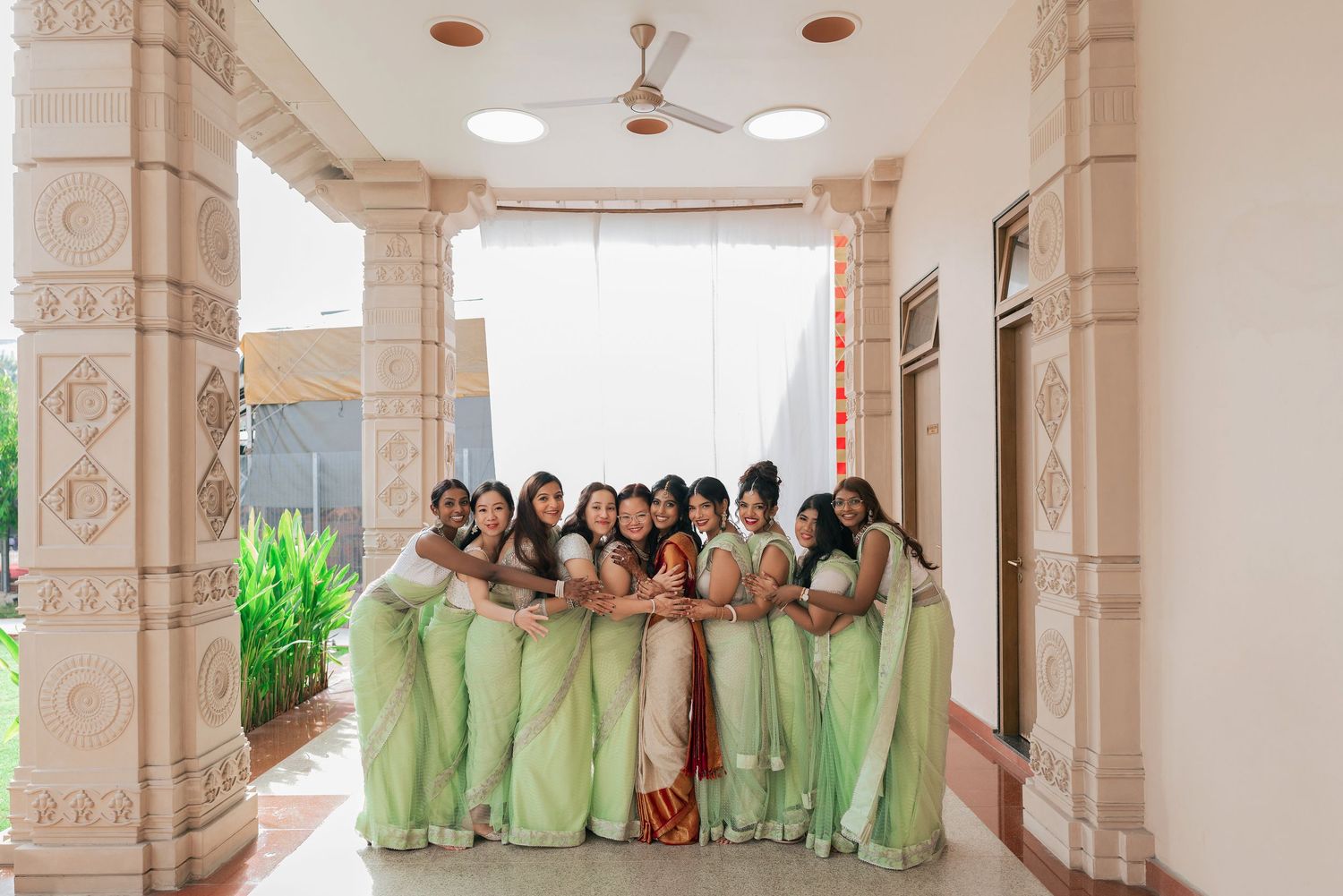 A group of bridesmaids in matching light green sarees posing together under ornate columns at an Indian wedding venue.