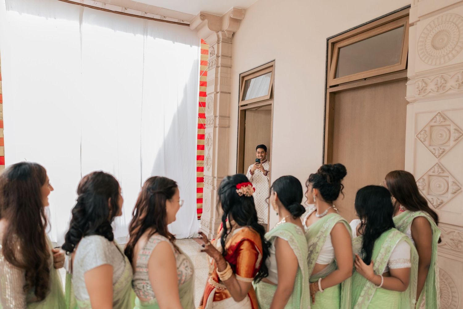 Bridesmaids in mint green sarees gather around a bride in red and gold at an Indian wedding ceremony.