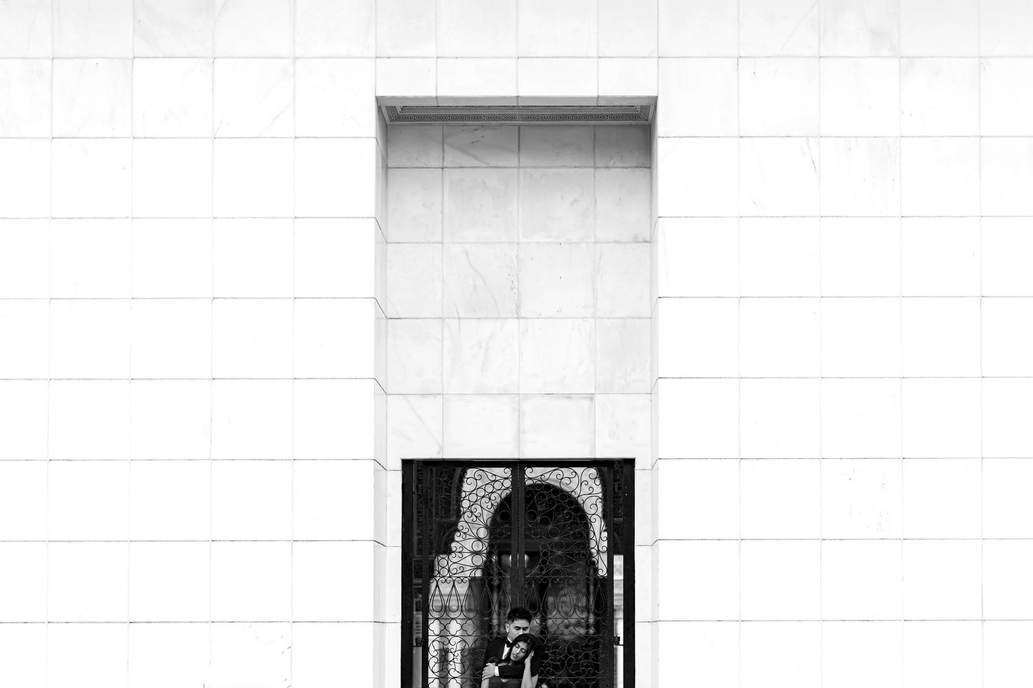 Black and white photo of a person standing in an ornate arched doorway set within a large white marble wall.