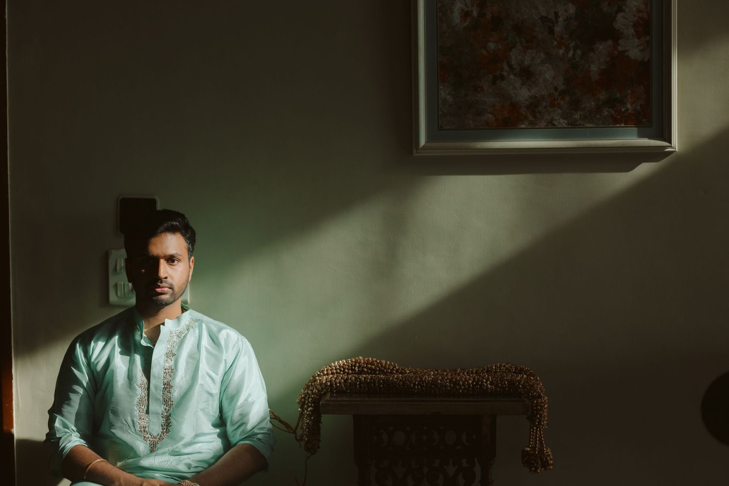 A person in a light blue button-down shirt sits in a moody, dark room illuminated by dramatic window light.