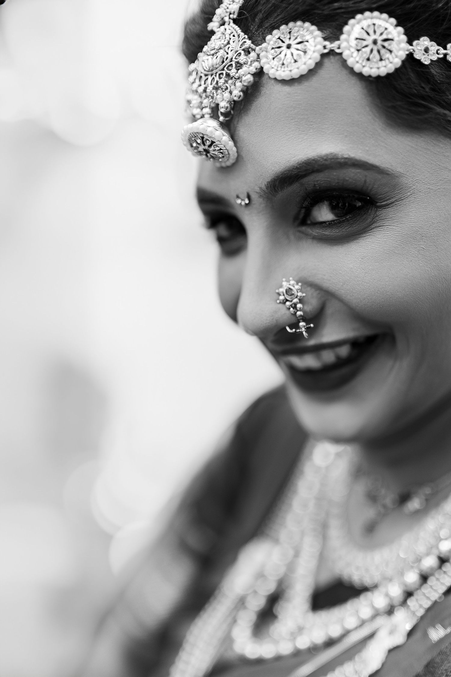 Black and white close-up portrait showing elegant pearl necklace and traditional bridal jewelry details.