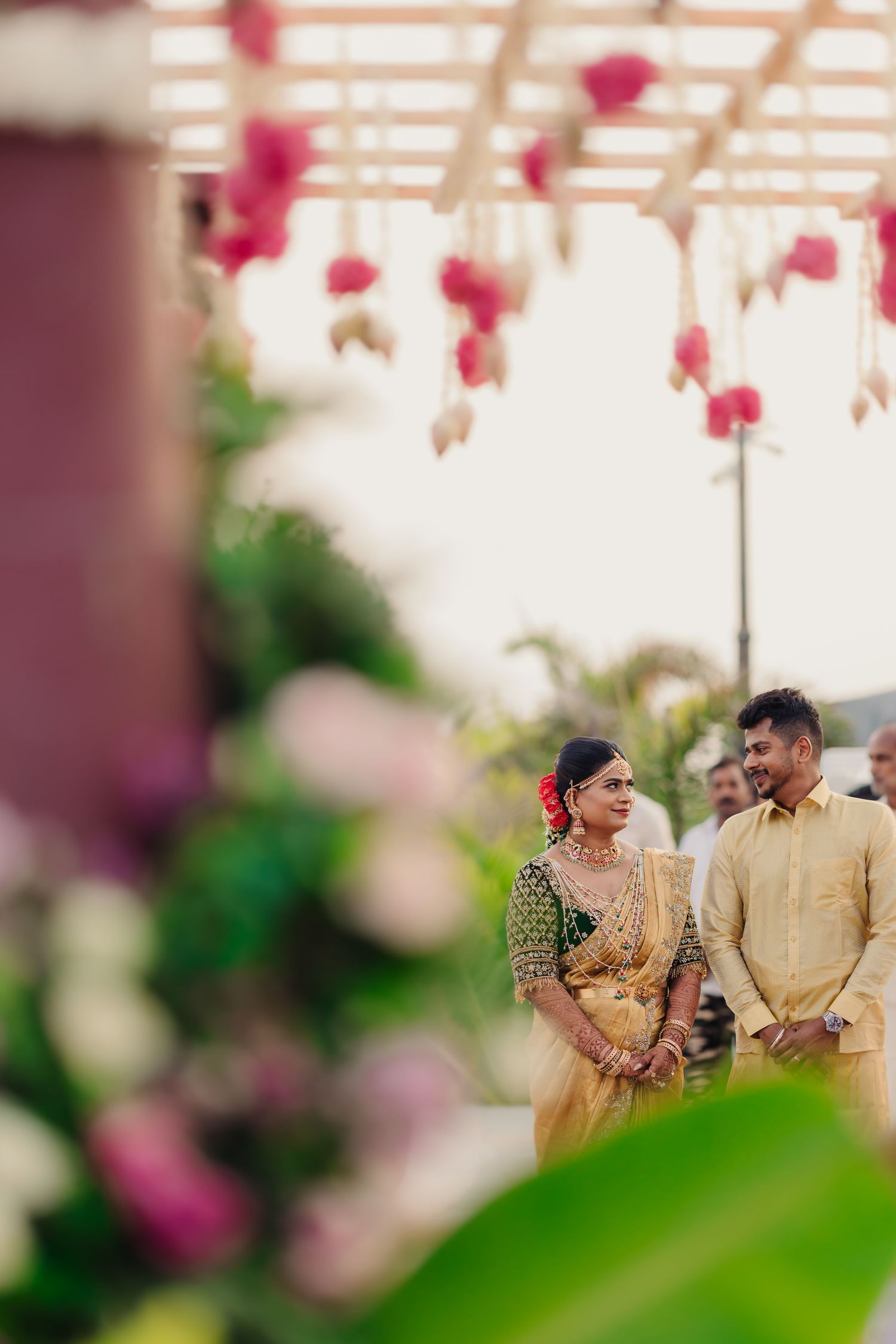 Couple in traditional Indian attire sharing a moment under pink floral decorations at a wedding ceremony.