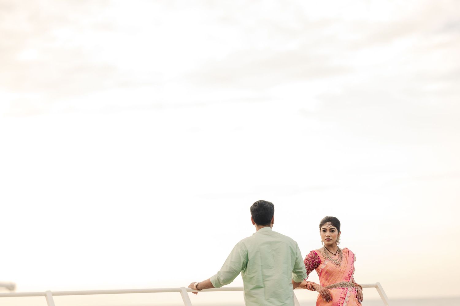 A couple in traditional Indian attire poses together in a romantic outdoor photoshoot at sunset.