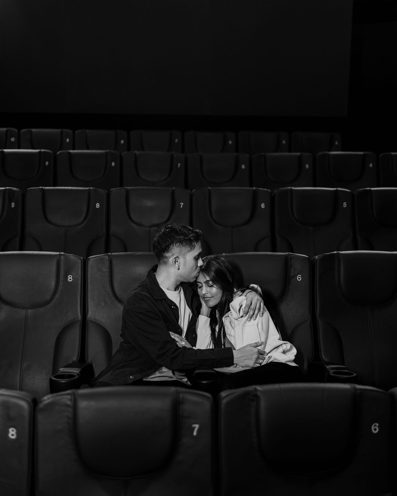 Black and white photo of a romantic couple embracing in empty cinema seats.