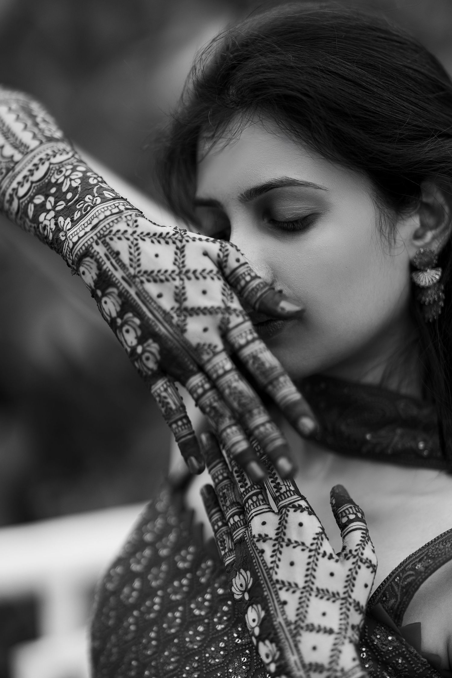 Black and white artistic photo of hands decorated with intricate henna designs covering the face in a traditional style.