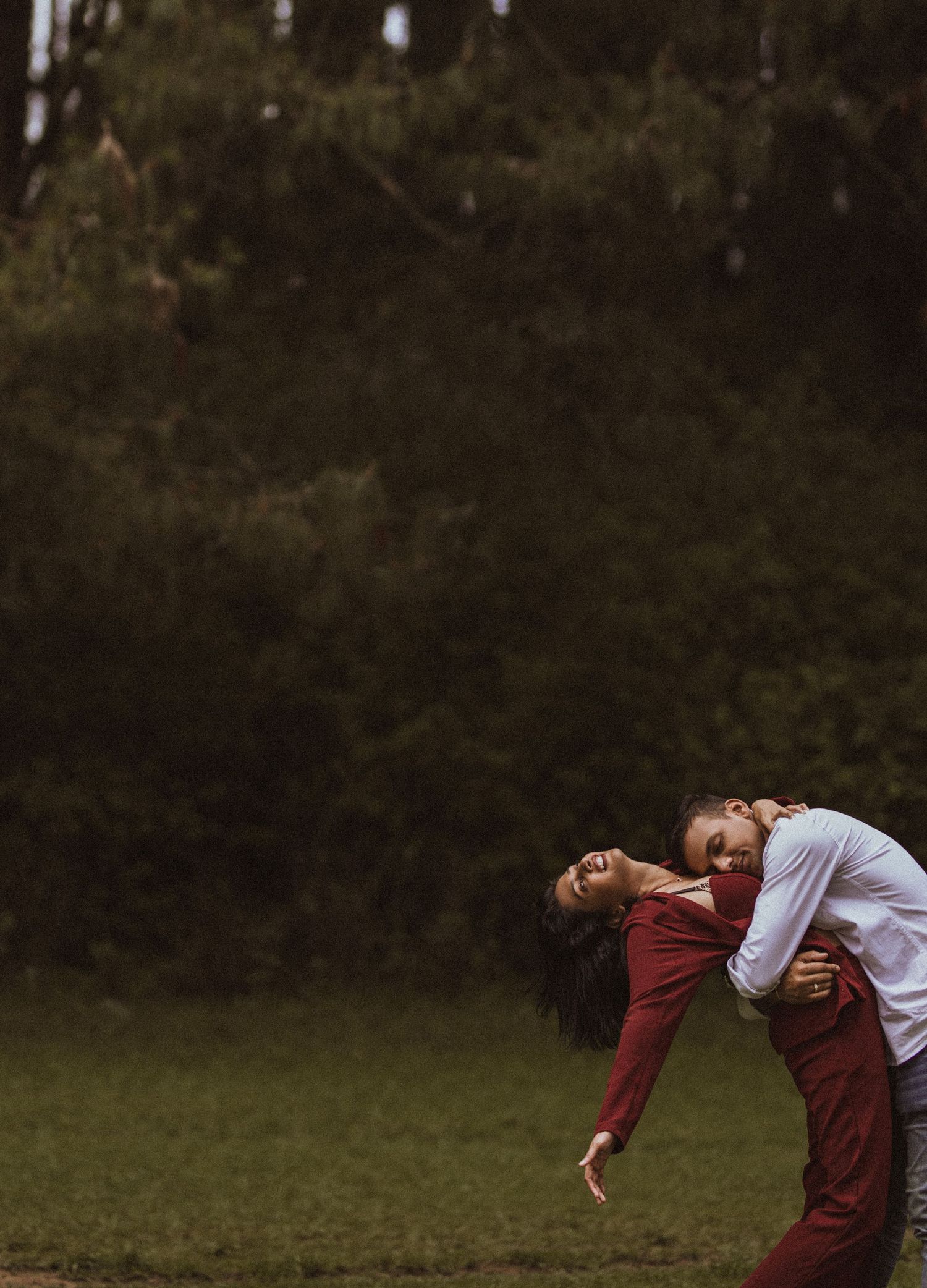 A person in a burgundy sweater and white shirt performs a graceful backbend on a grassy field at dusk.