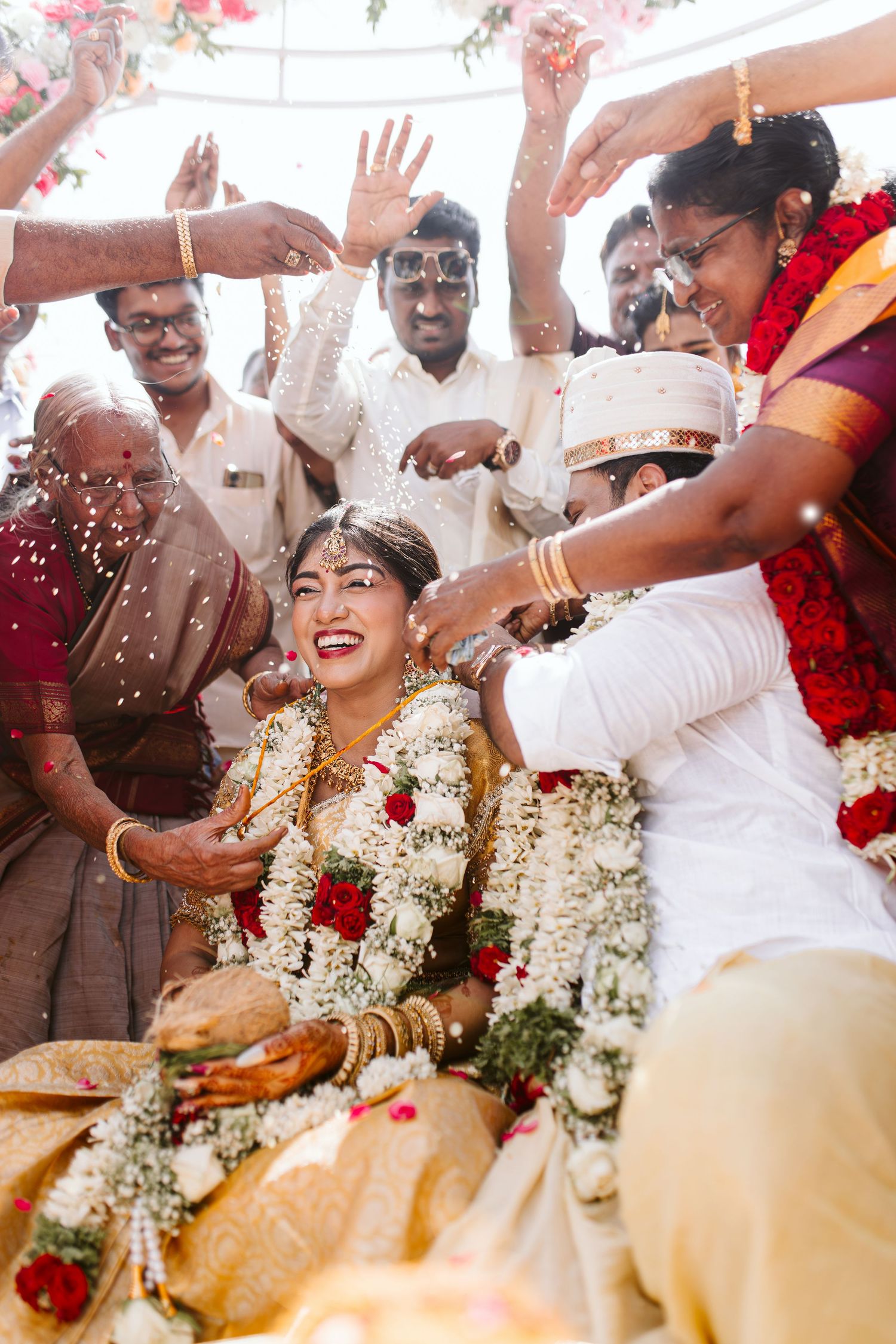 Wedding guests shower newlyweds with rice and flower petals during joyous traditional Indian marriage celebration.