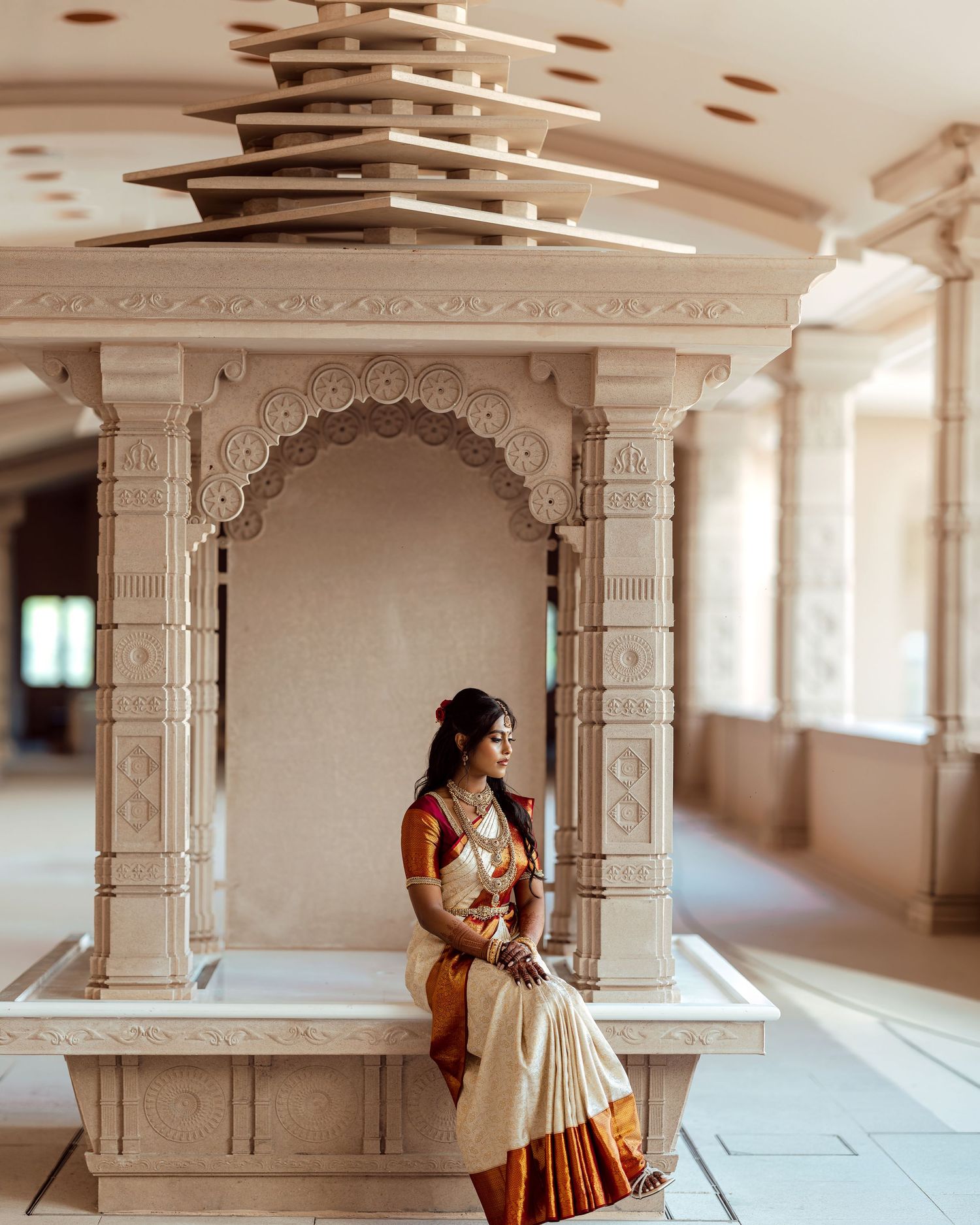 Woman in traditional Indian saree sitting gracefully inside an ornate Hindu temple shrine with white marble architecture.
