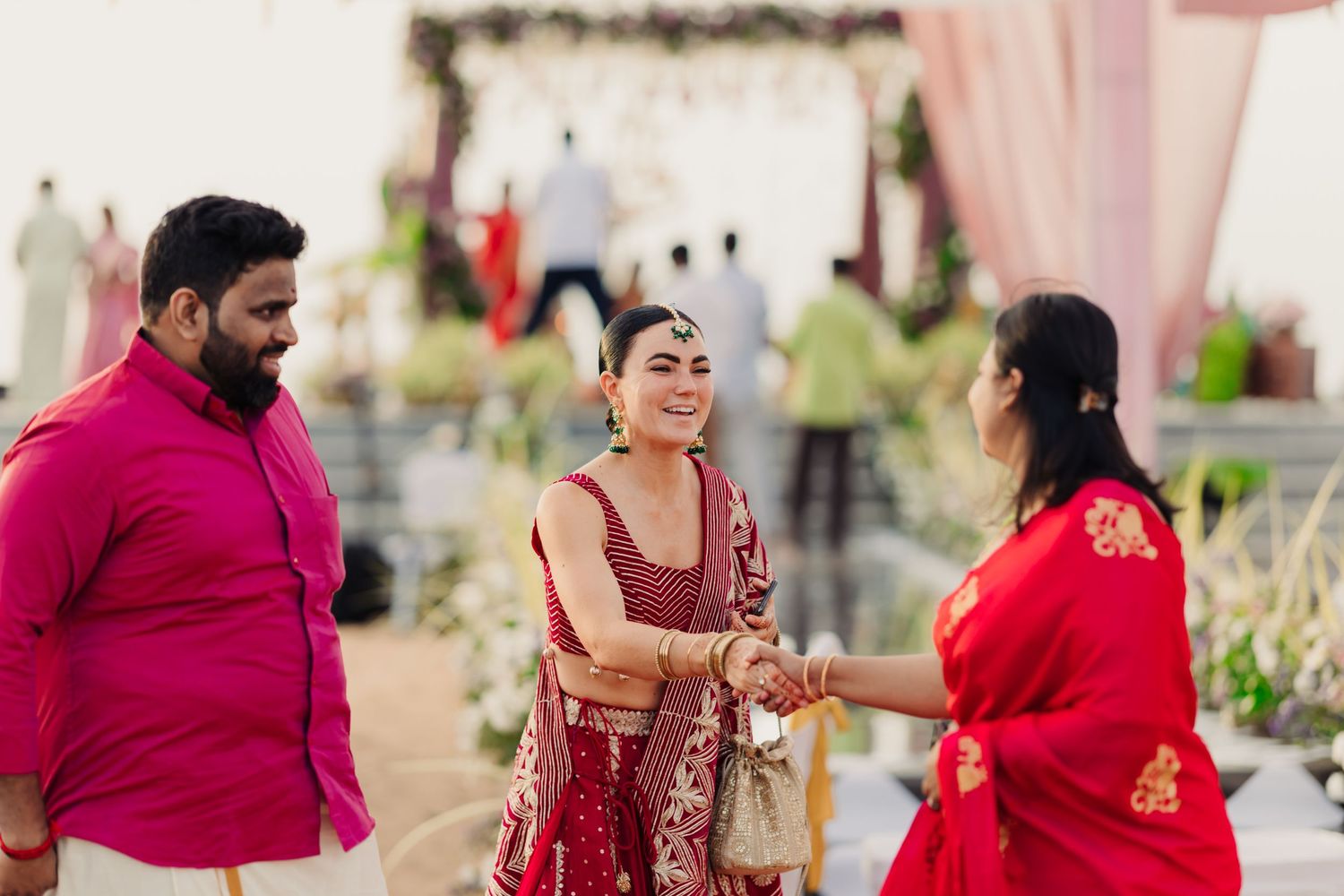 People in traditional Indian attire share a joyful moment at an outdoor celebration decorated with floral arrangements.