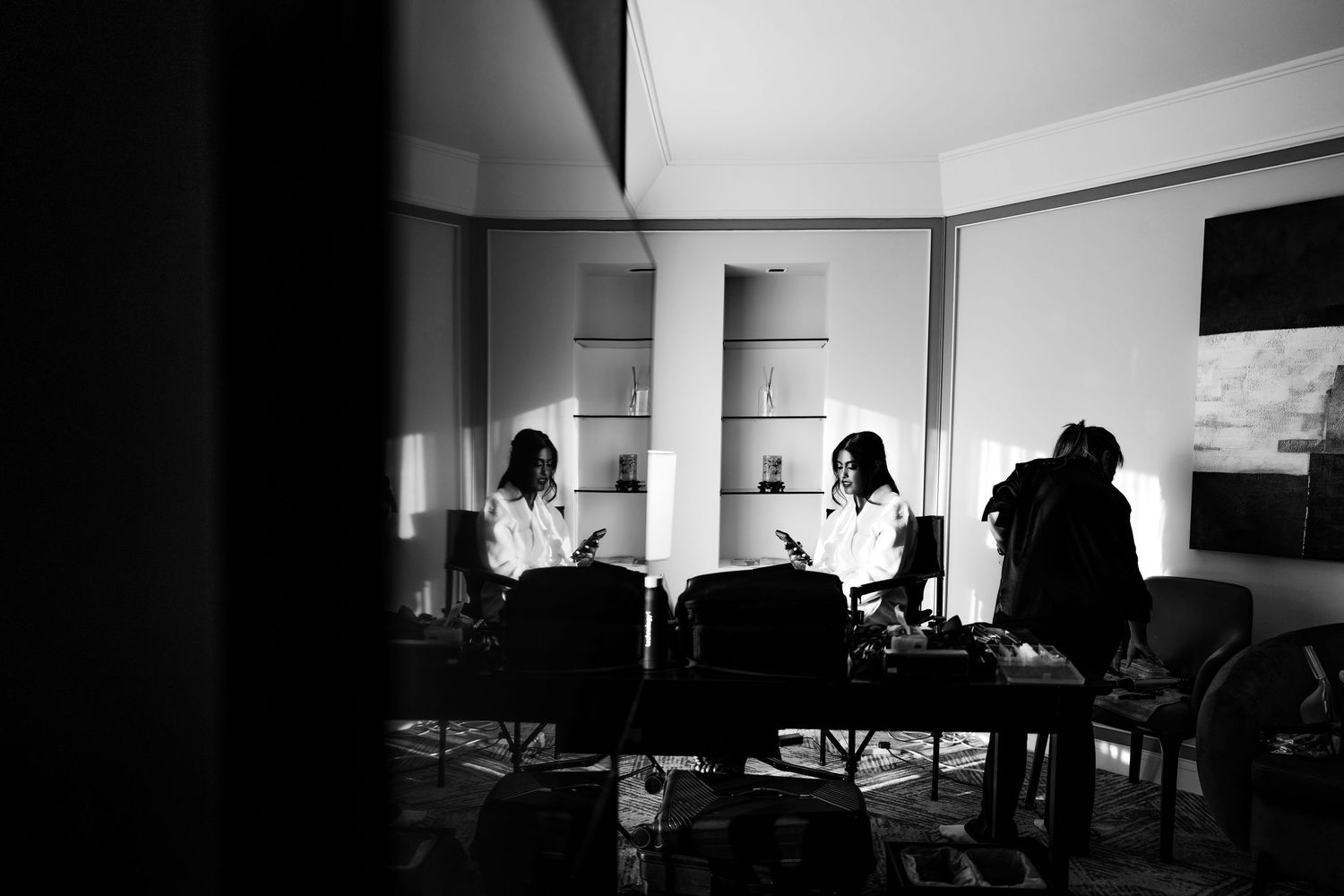 Black and white photo of two women sitting in chairs in a bright room, captured through a doorway.