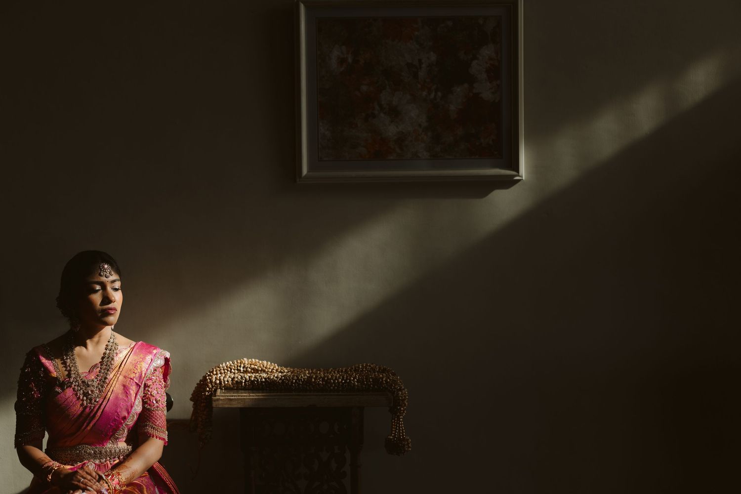 A person in a pink dress stands in a dimly lit room with dramatic shadows and light beams streaming through a window.